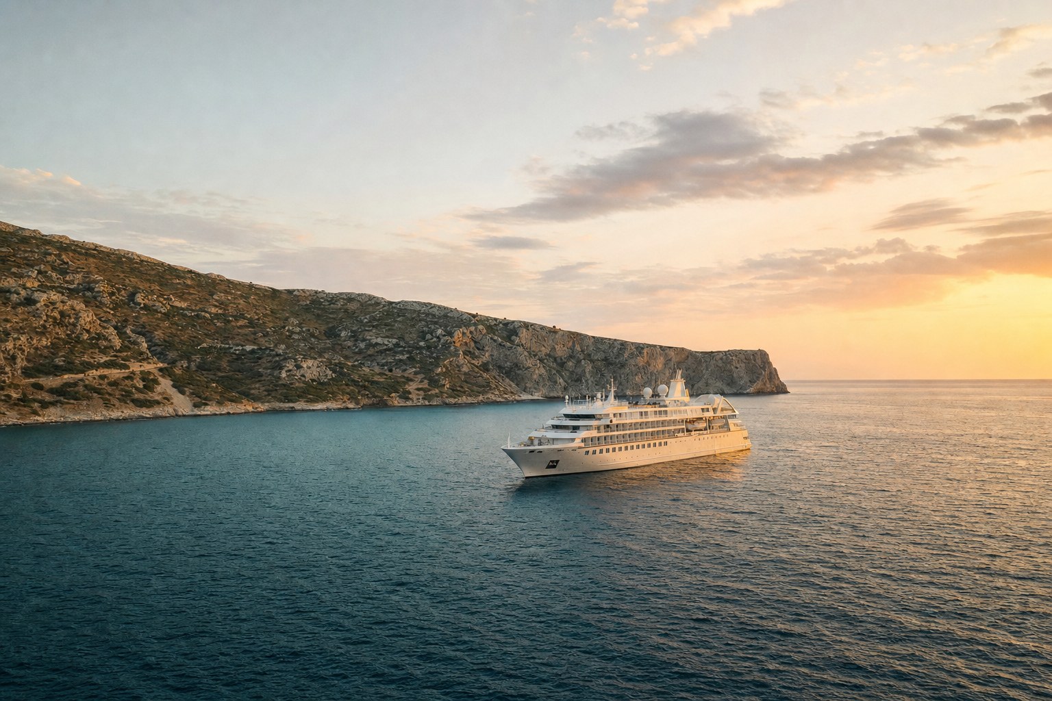 Small luxury cruise ship sailing along a quiet coastline at sunset