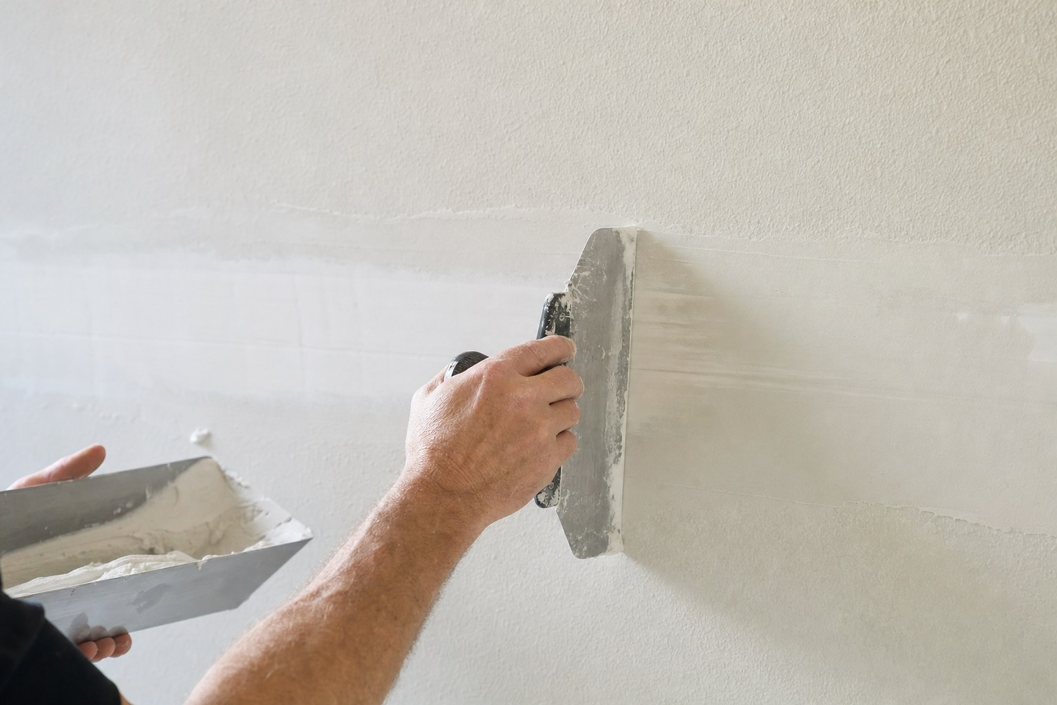 Hands applying joint compound across a textured drywall seam