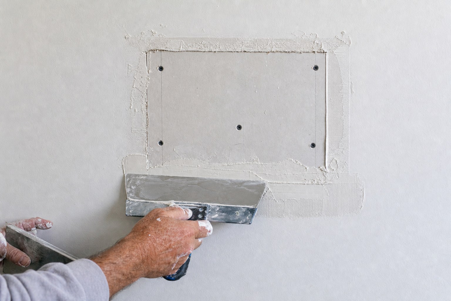 Drywall patch being finished with joint compound