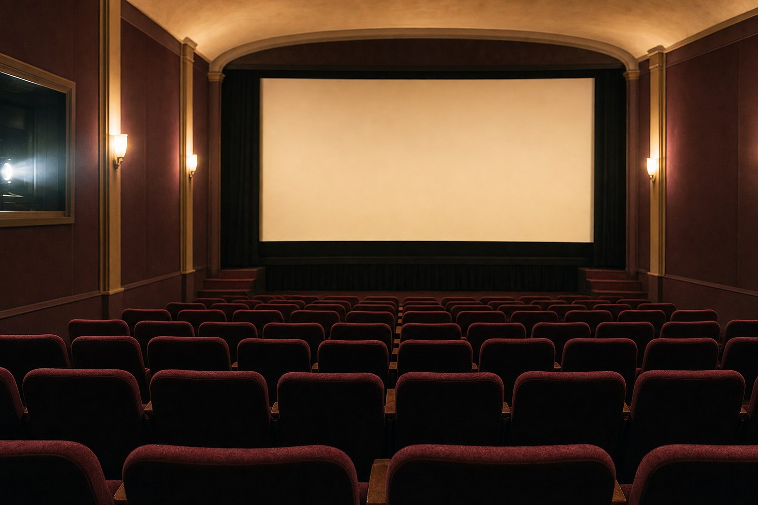 An empty cinema with a softly lit blank screen and burgundy seats
