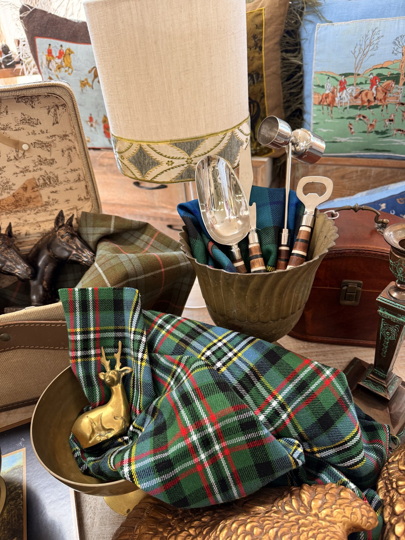 Tartan textile, brass deer, equestrian cushions, and a vintage train case