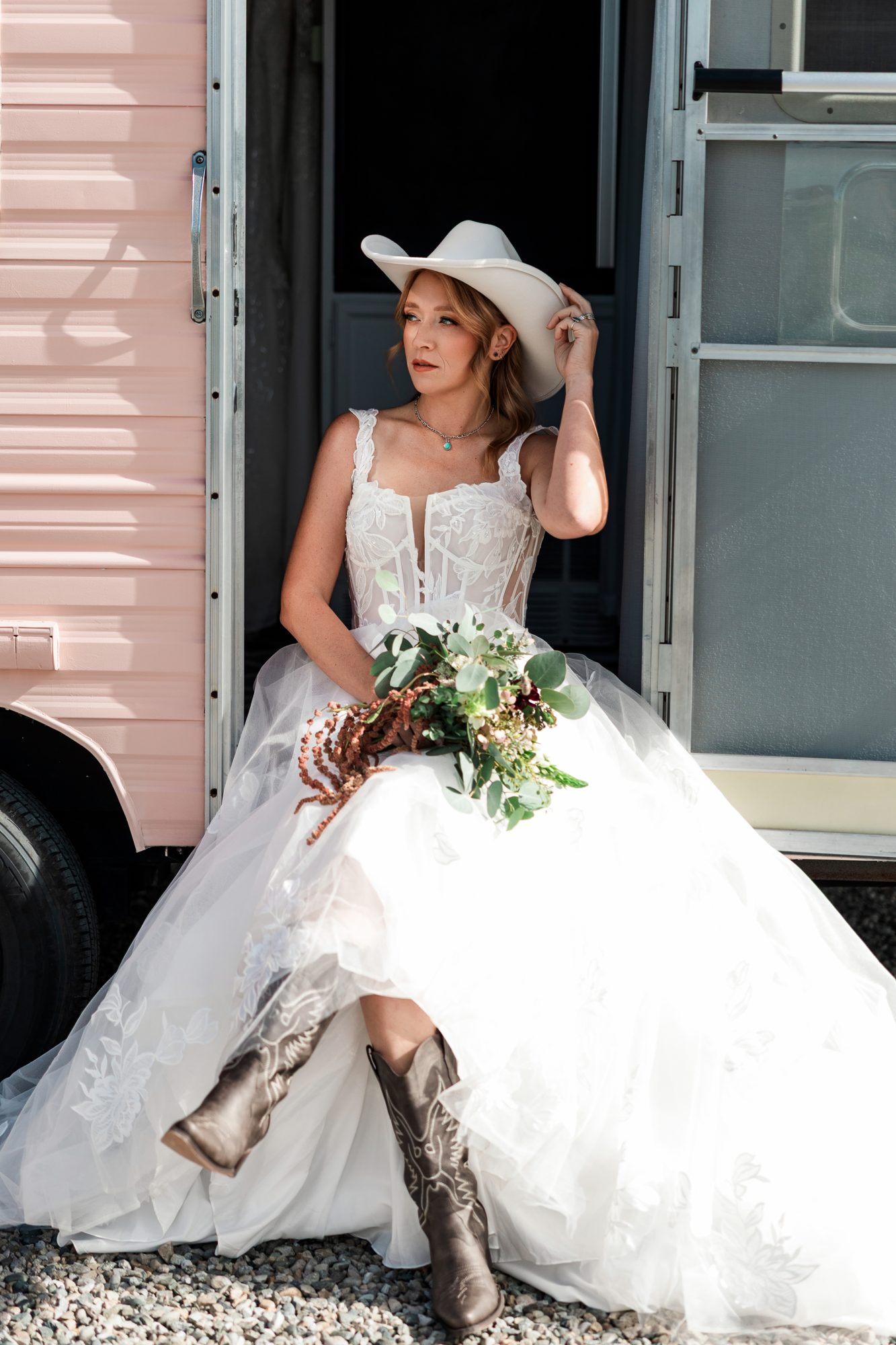 Bride in a lace wedding gown and western boots, seated in the pink bridal suite doorway