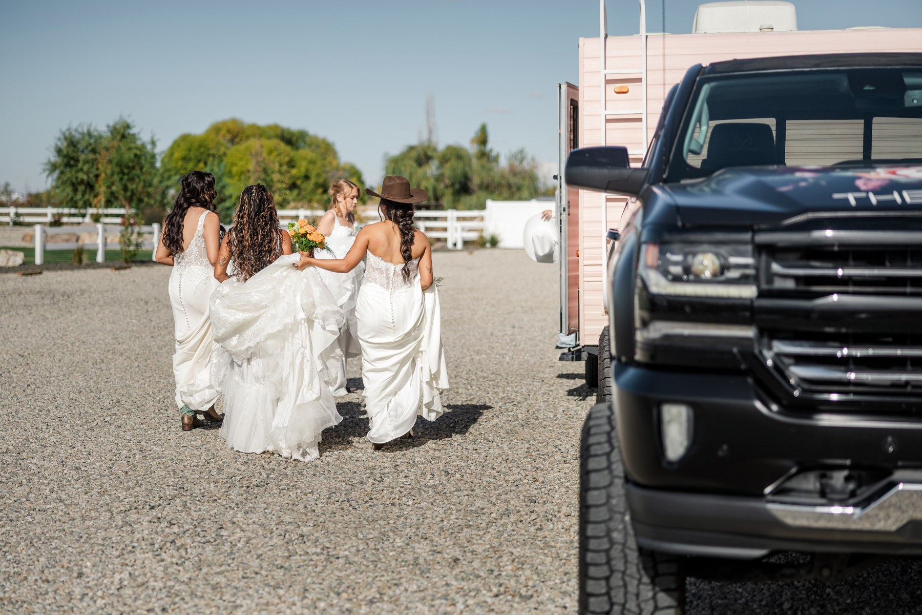 Four brides walking together in wedding gowns beside The Bustle mobile bridal suite and truck