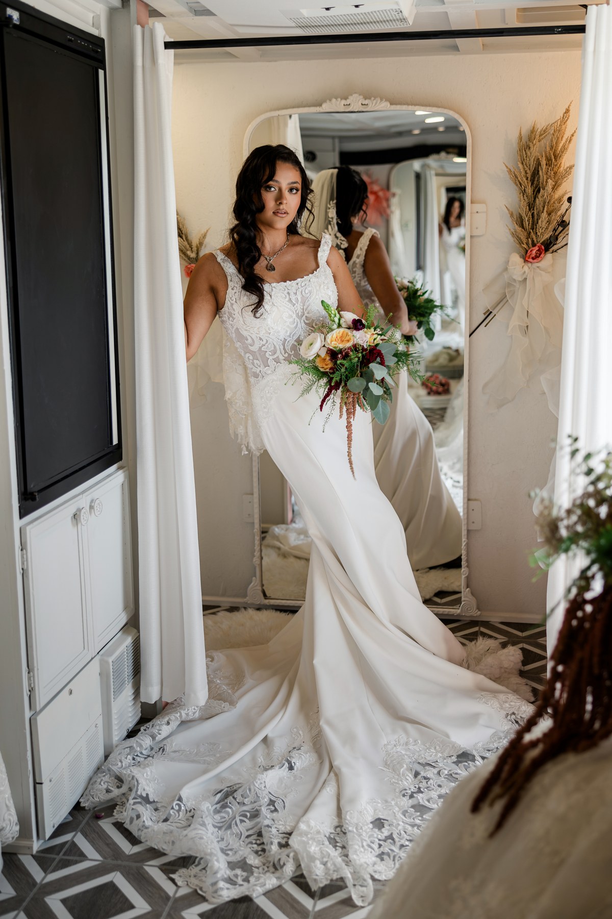 Bride in a fitted wedding gown with a lace bodice and flowing lace-edged train inside the mobile bridal suite