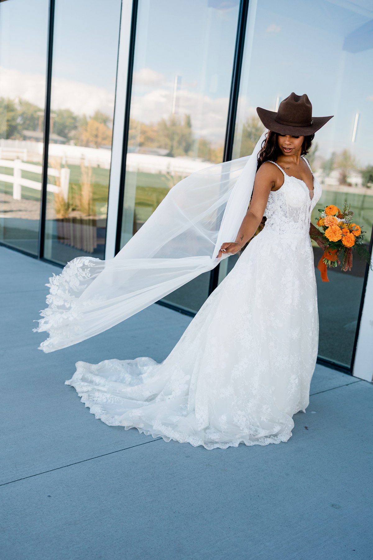 Bride in a lace wedding gown and brown hat with her veil sweeping to the side