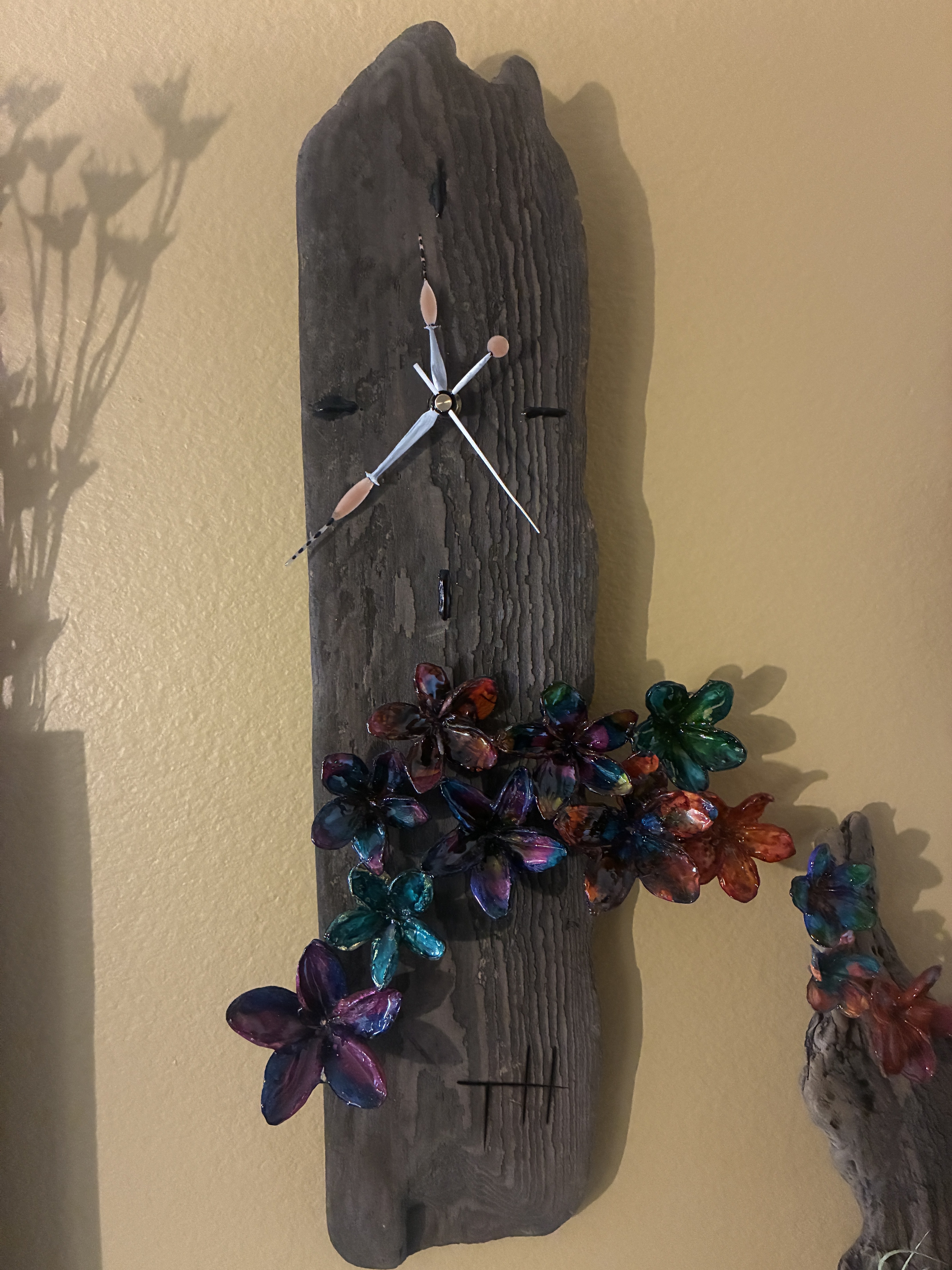 Handmade dark wood wall art with colorful resin flower forms in warm sunlight