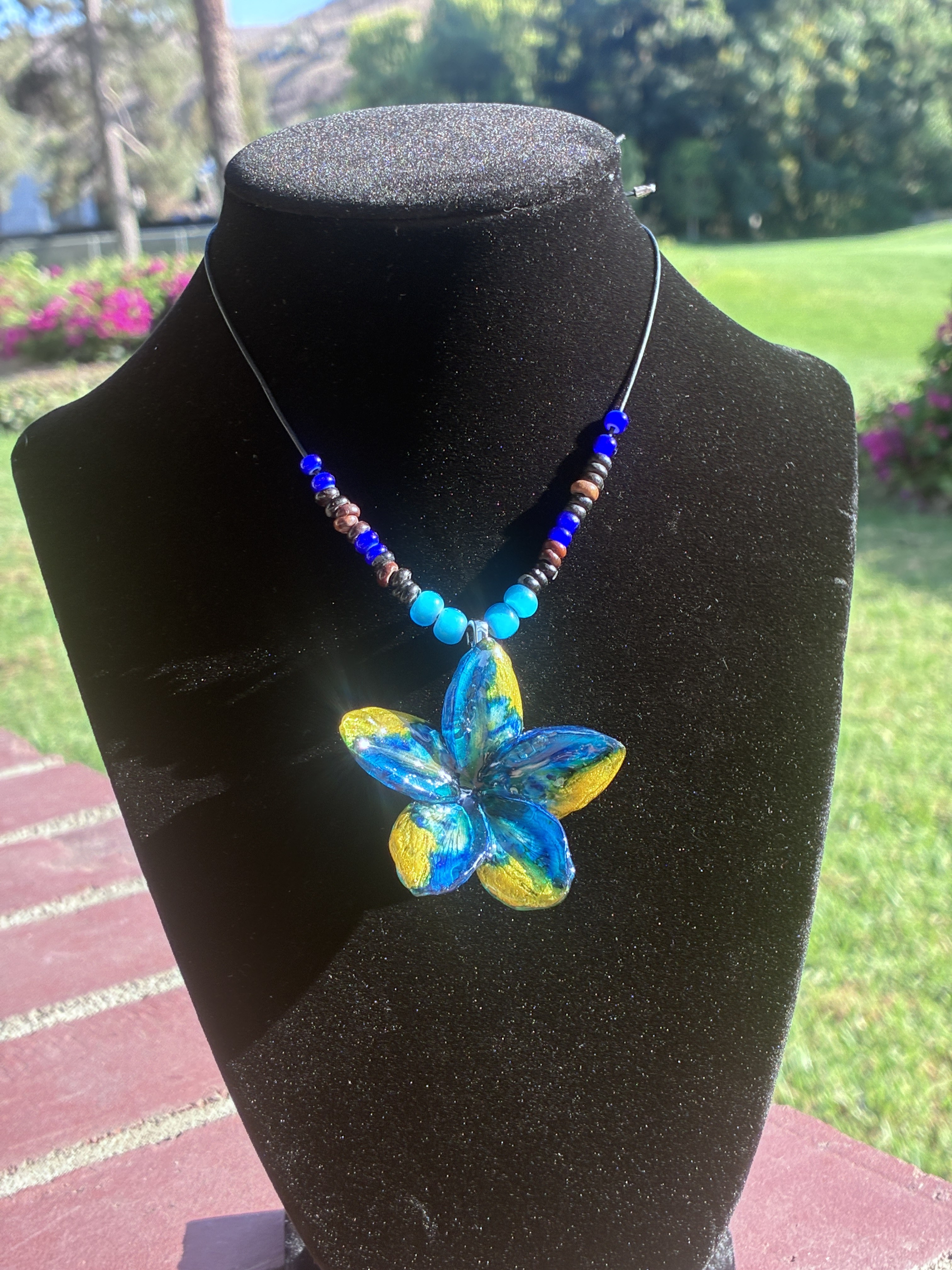 Blue and yellow floral handmade necklace displayed on a black jewelry bust