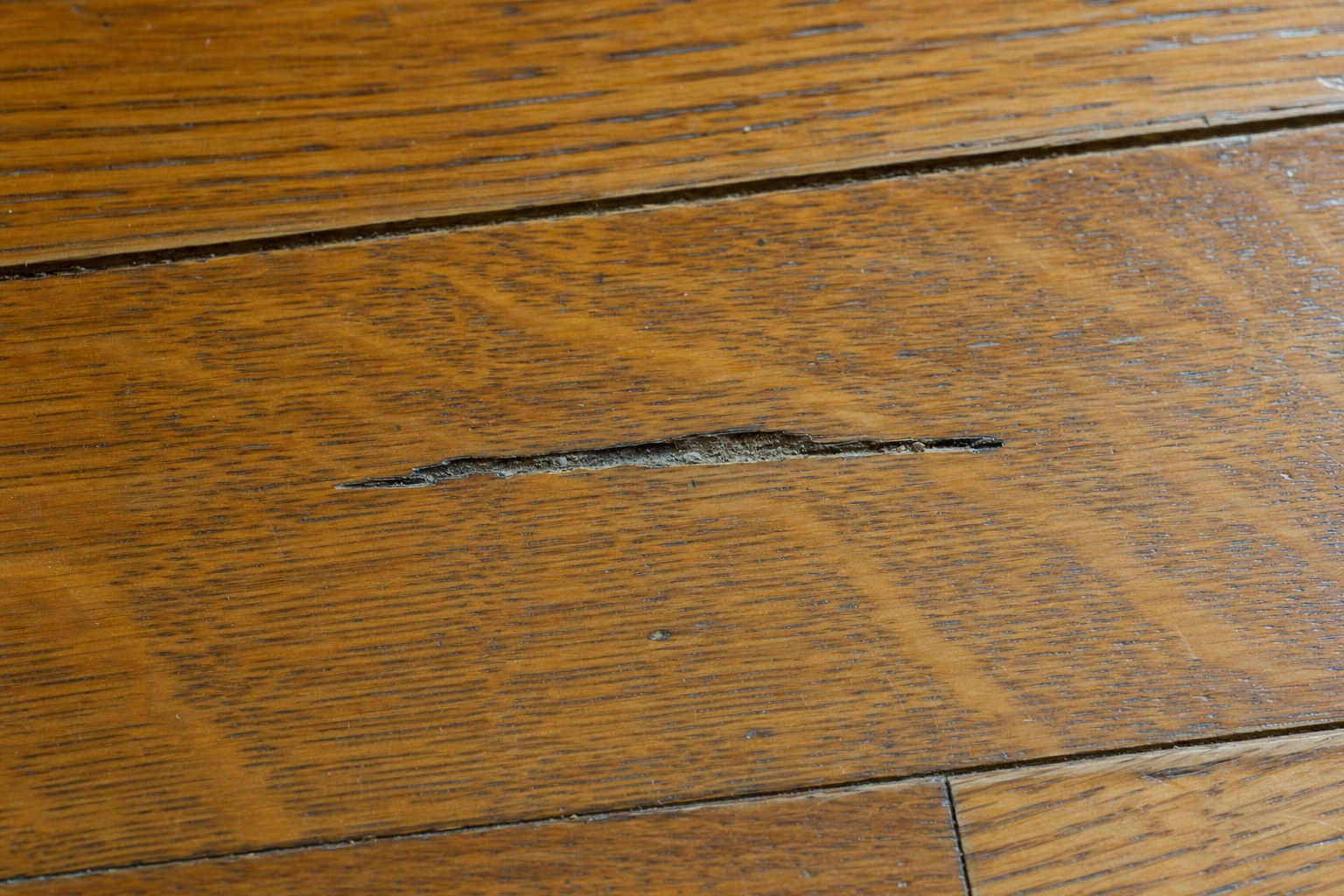 Deep narrow gouge visible in a warm oak hardwood floor