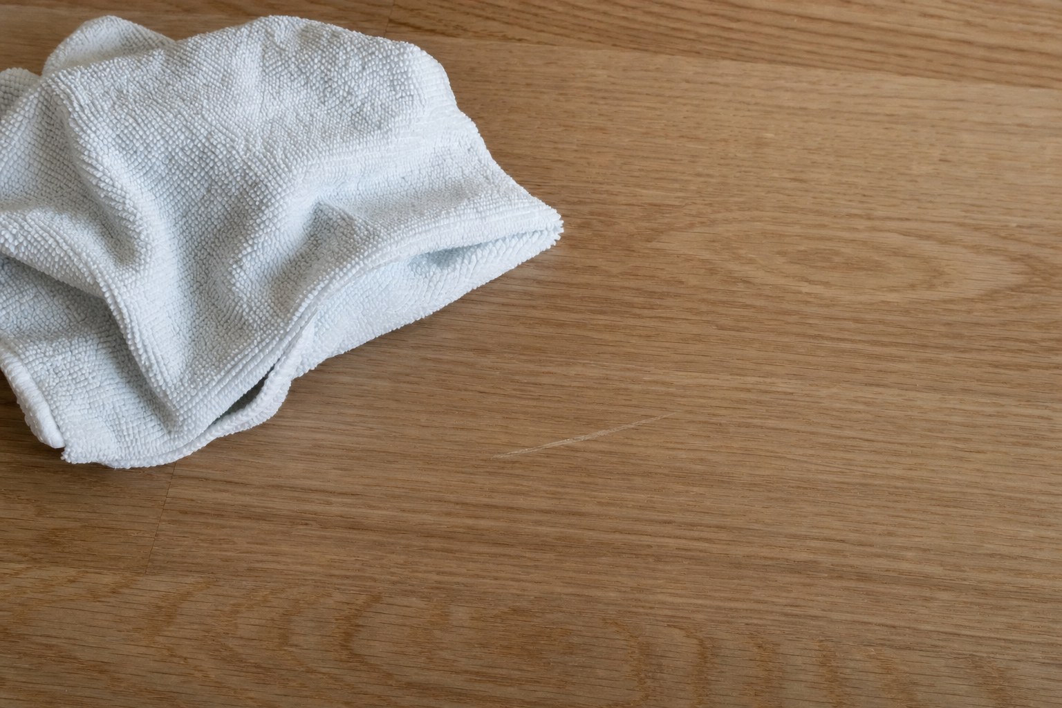 Microfiber cloth beside a faint surface scratch on a white oak hardwood floor