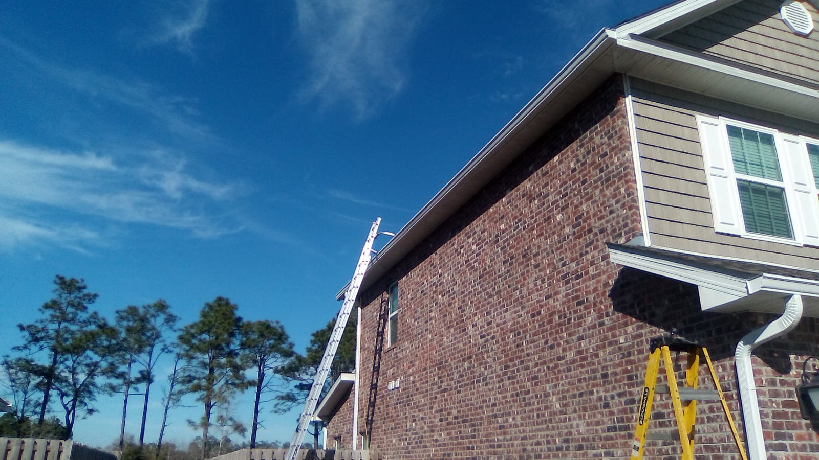 White seamless gutters being installed on a brick home