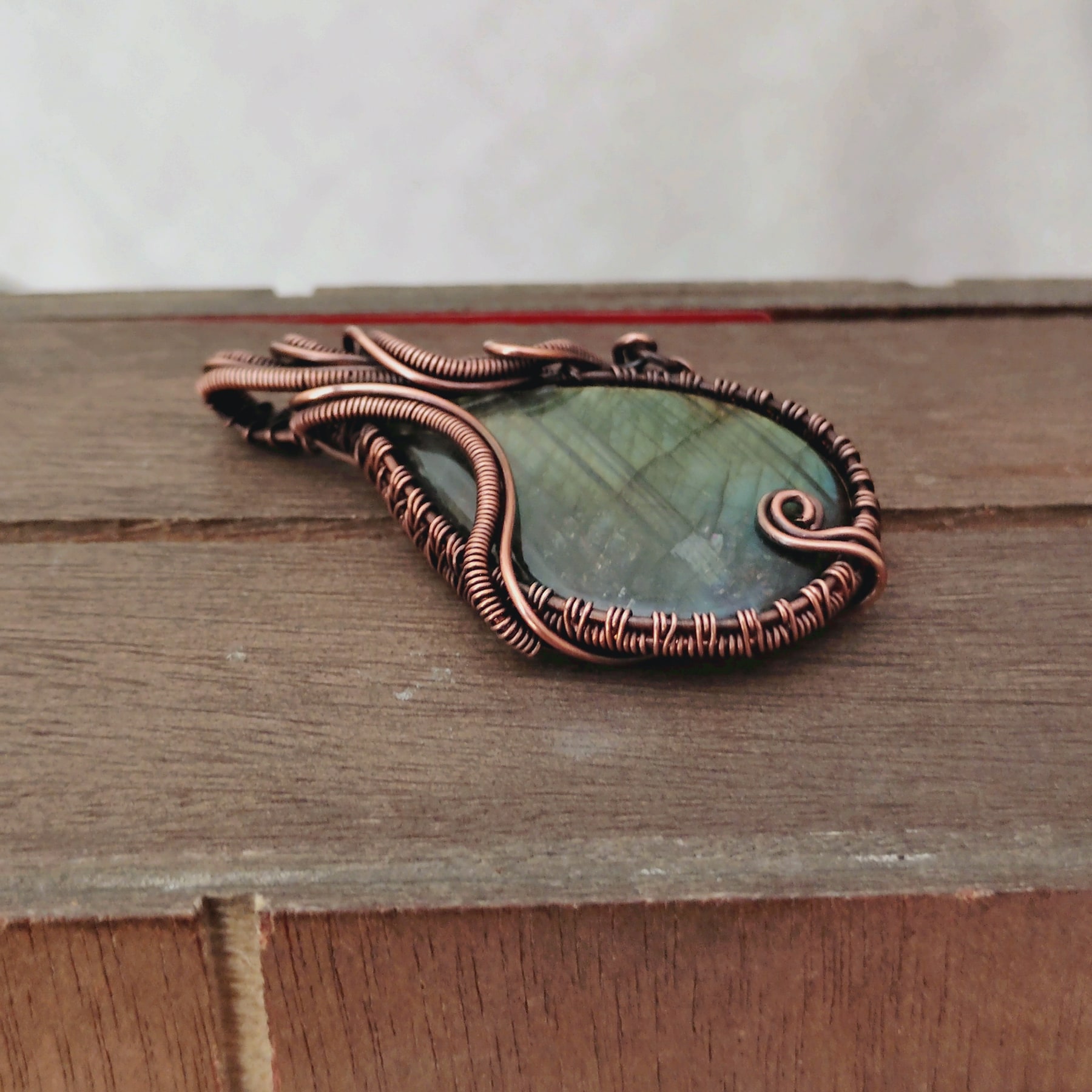Oxidized copper wire-wrapped labradorite pendant resting on wood