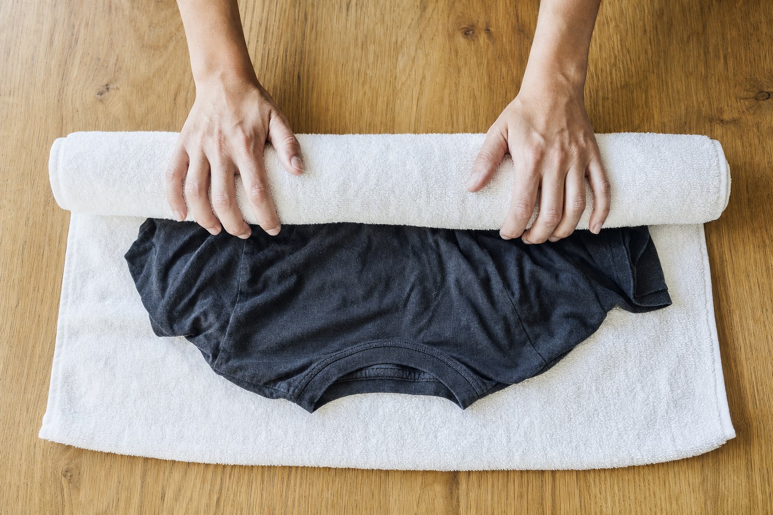 A dark cotton T-shirt being gently rolled in a white towel