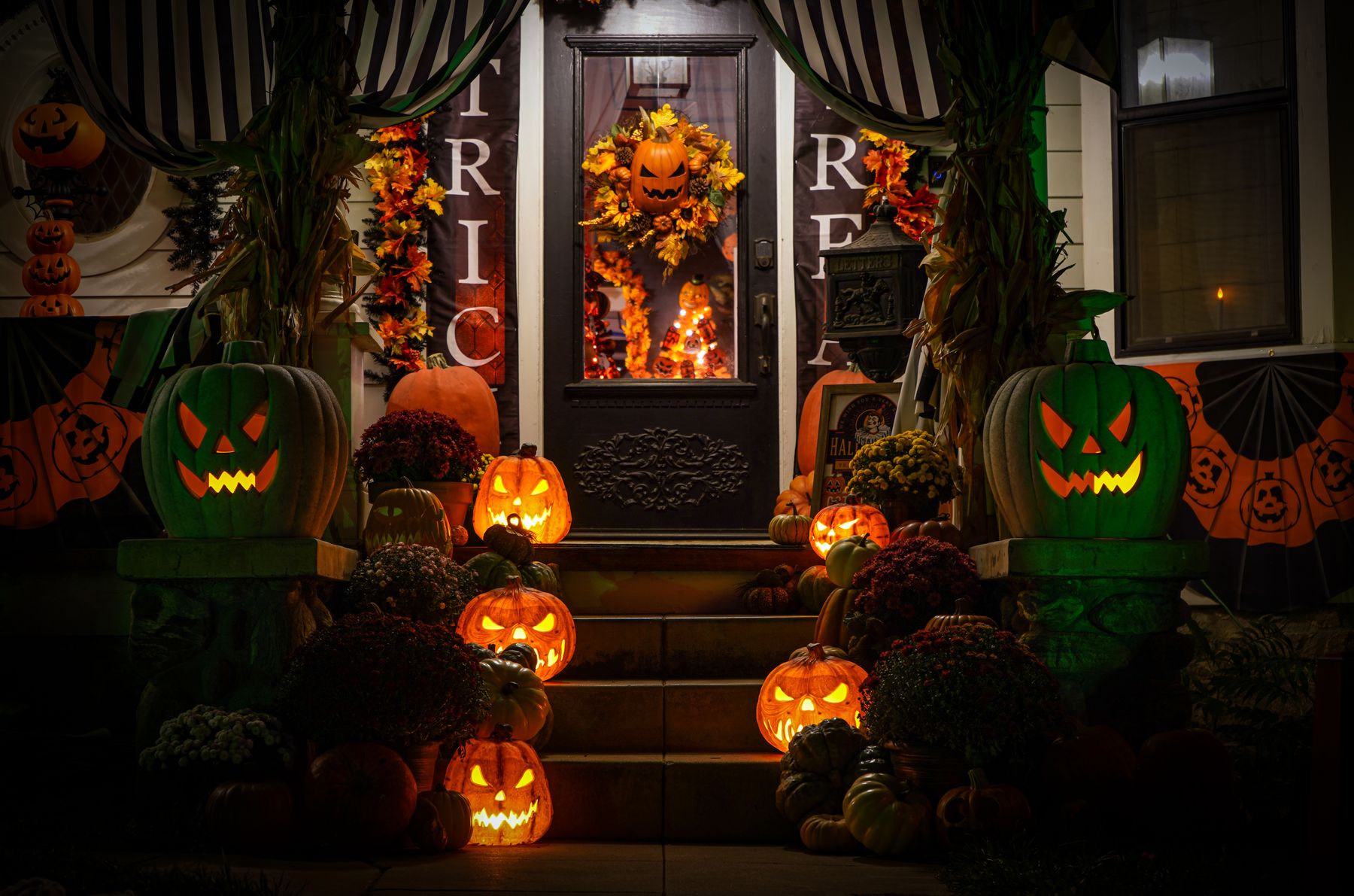 Halloween front porch with glowing pumpkins, decorations, and a dark front door at night