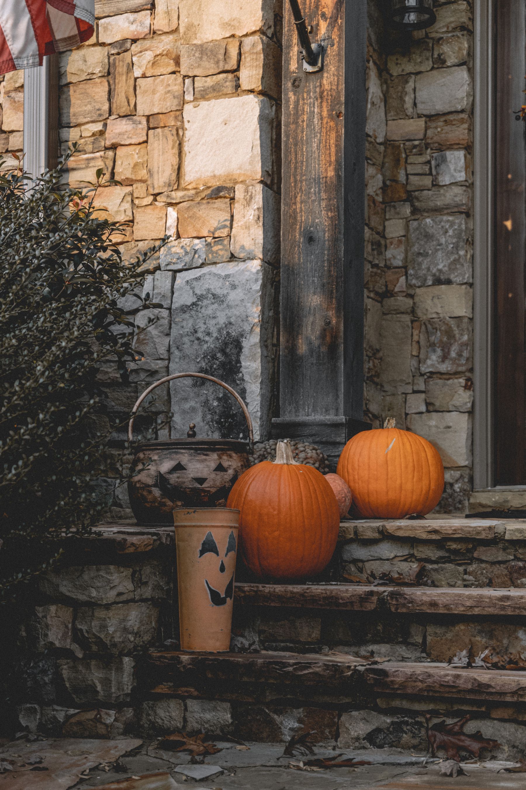 Pumpkins and a small jack-o-lantern bucket arranged beside stone front steps