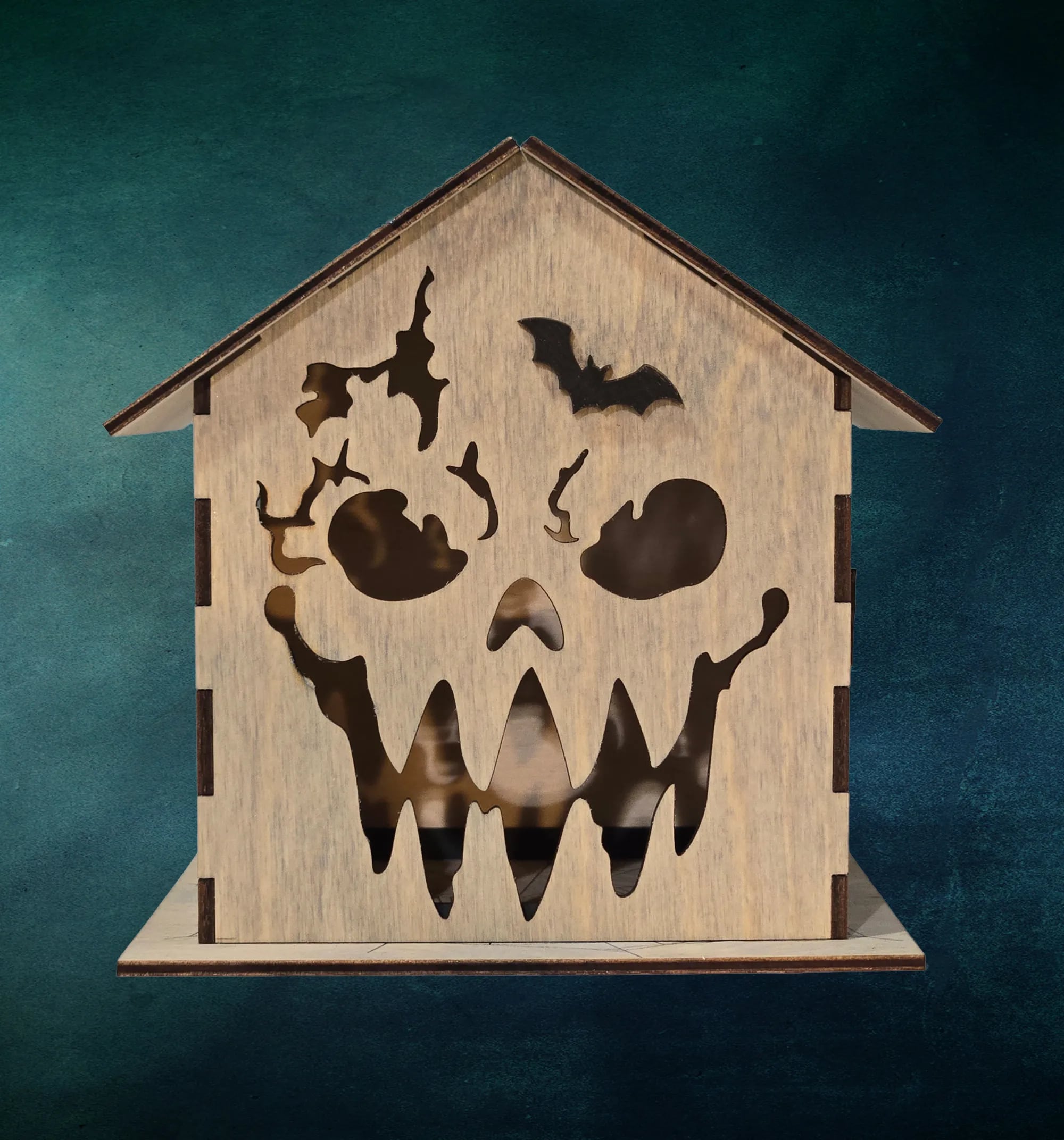 A laser-cut wooden Halloween house lantern glowing on a dark surface