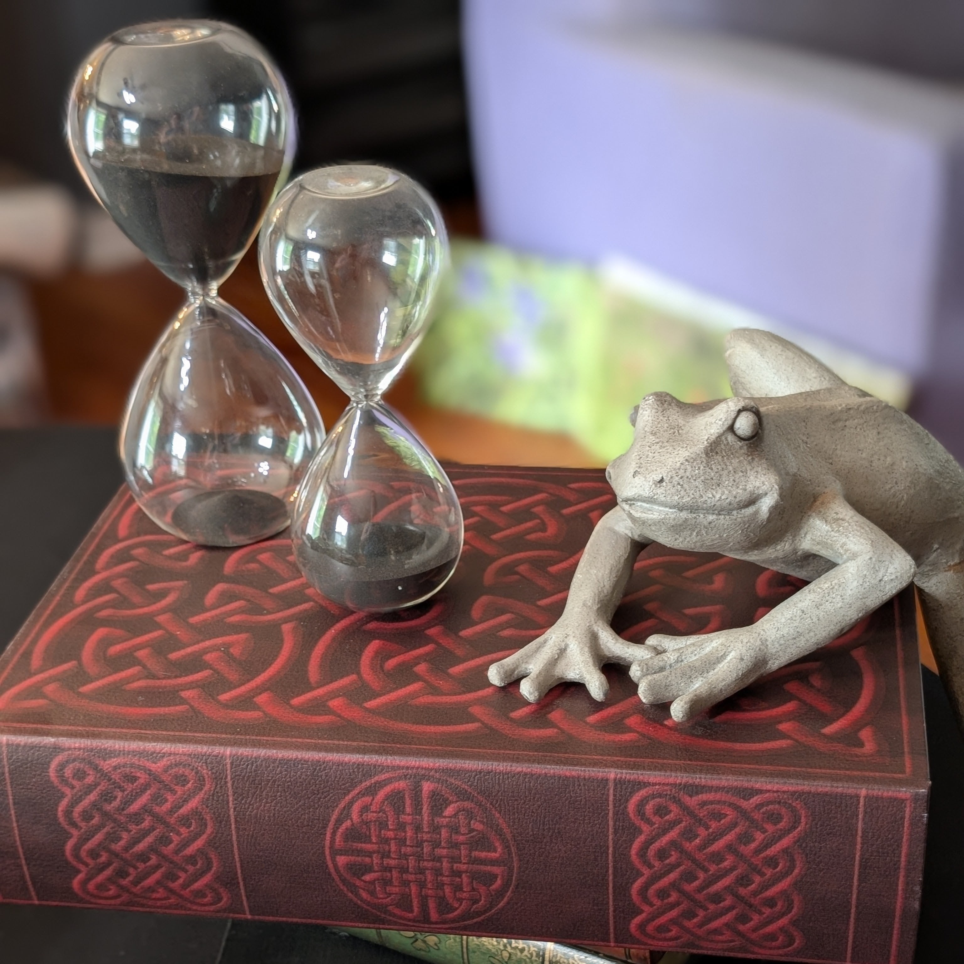 A frog beside a glass hourglass on a patterned red book