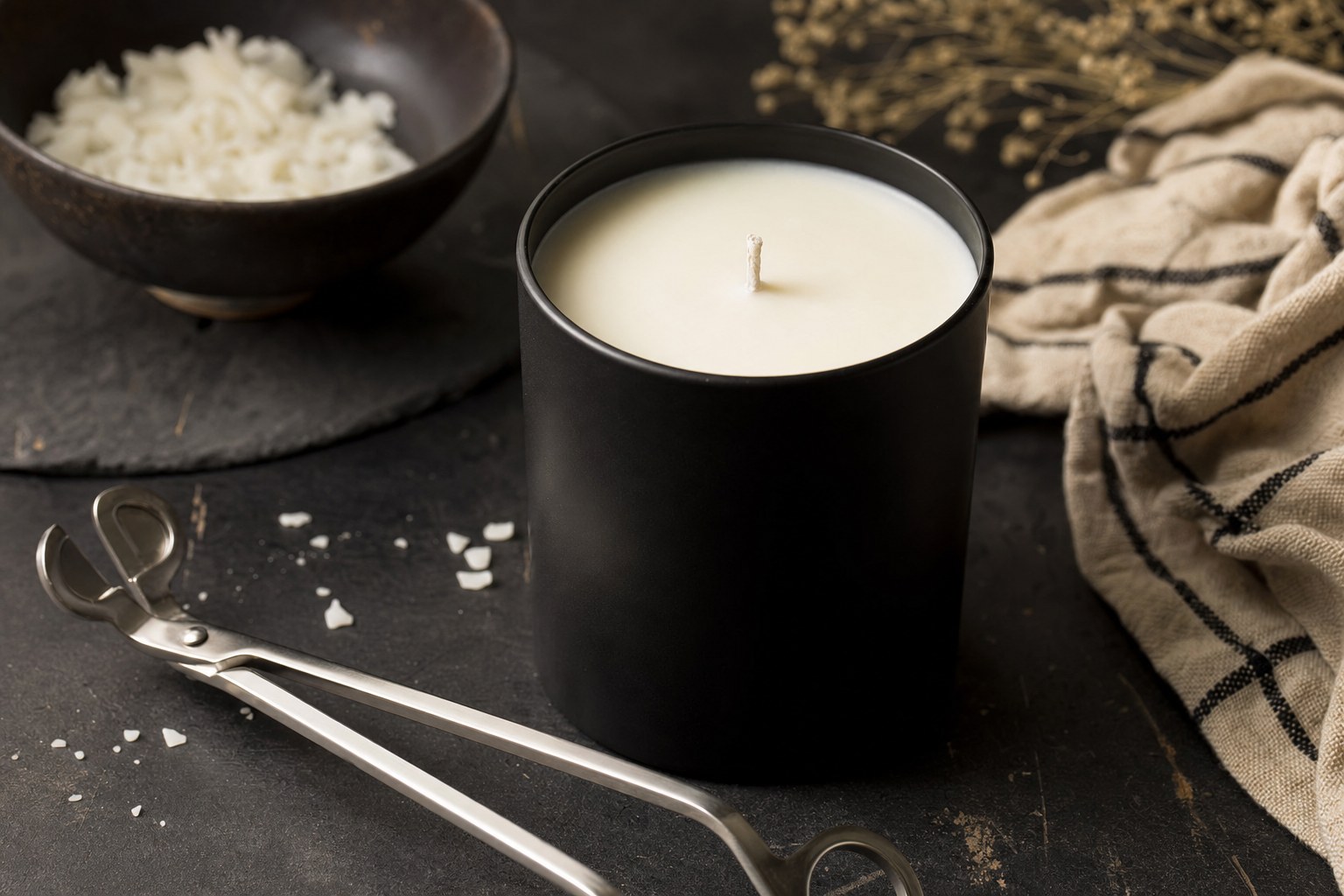 A wick trimmer beside an unlit black container candle.