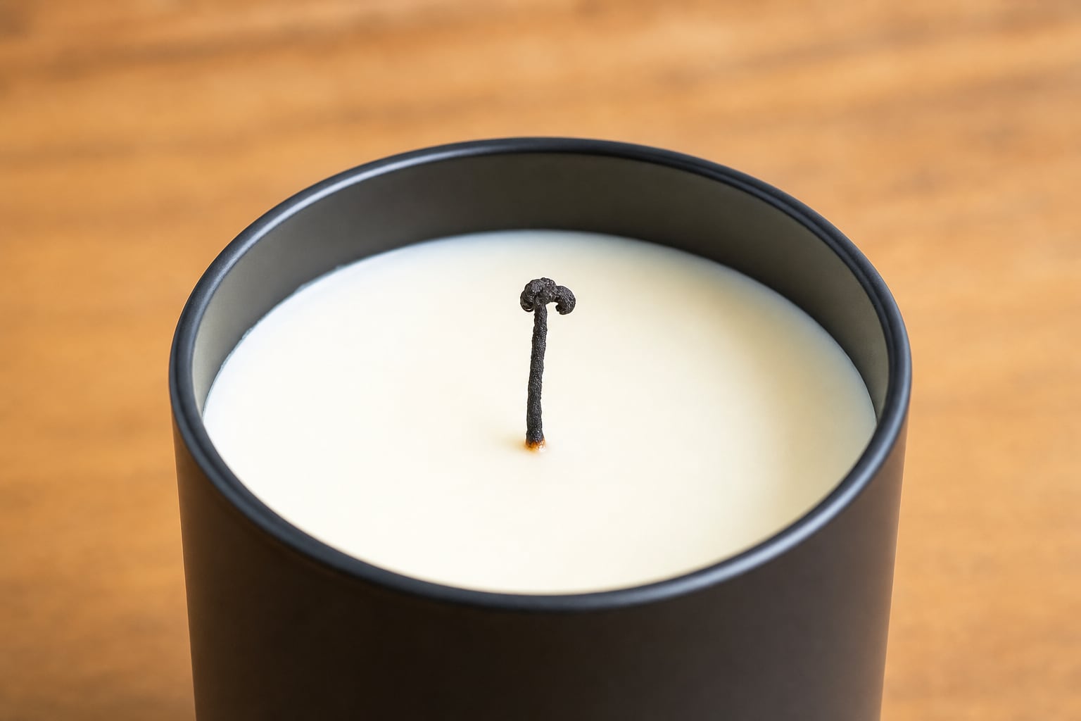 A cooled black container candle with a mushroomed wick ready to be trimmed.