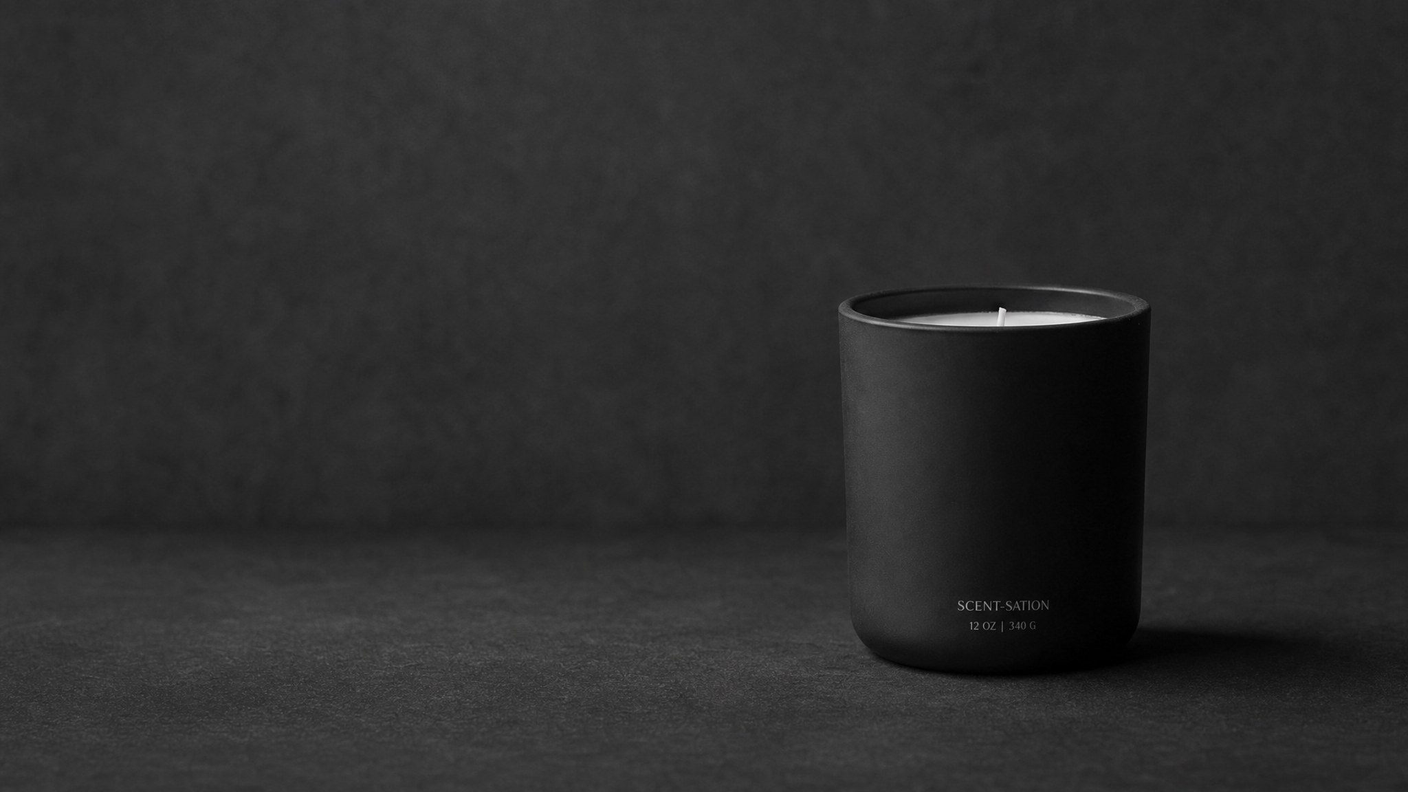 A hand-poured black container candle on a table.