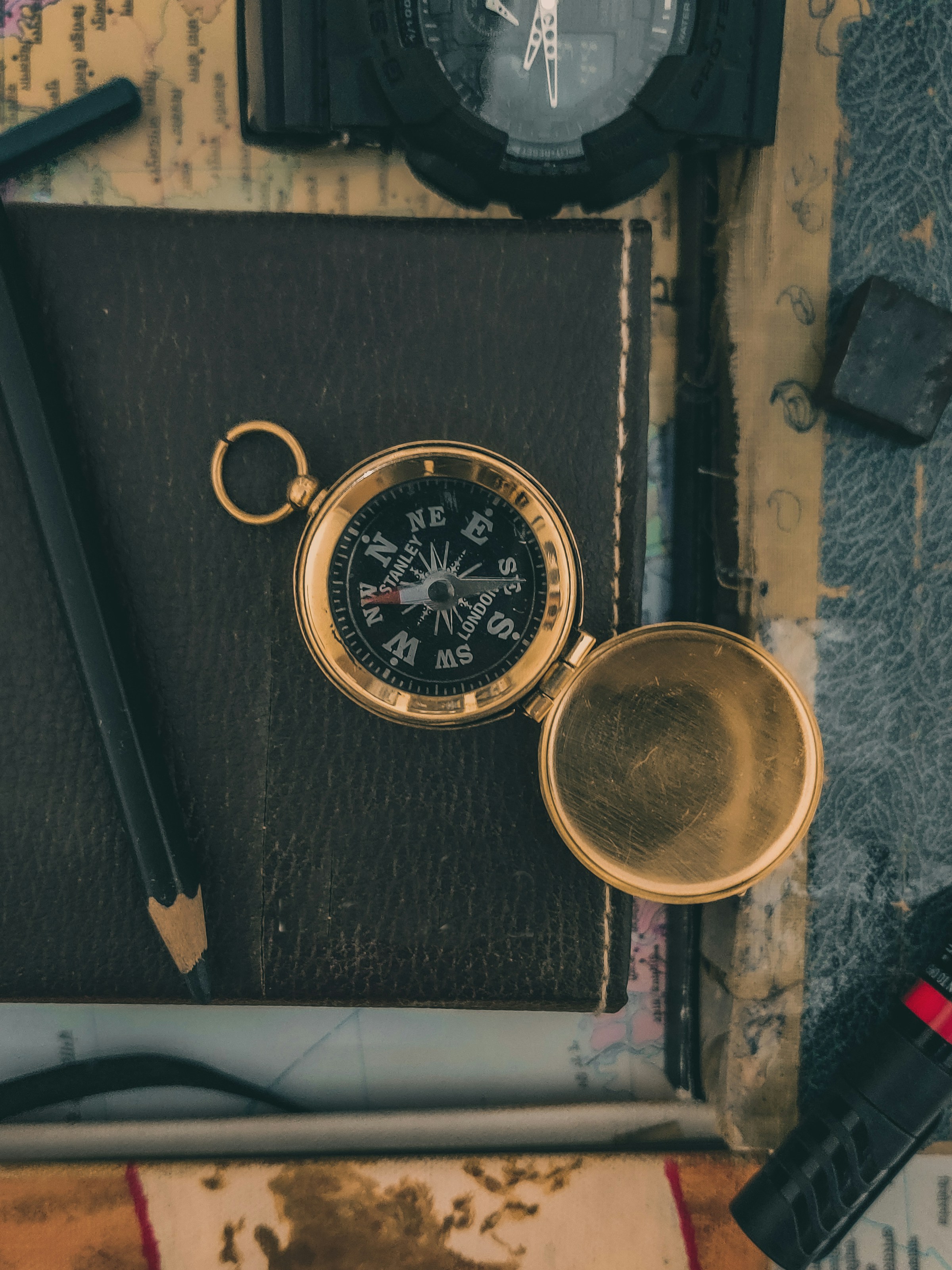 Compass and pocket watch resting on a dark notebook beside a map