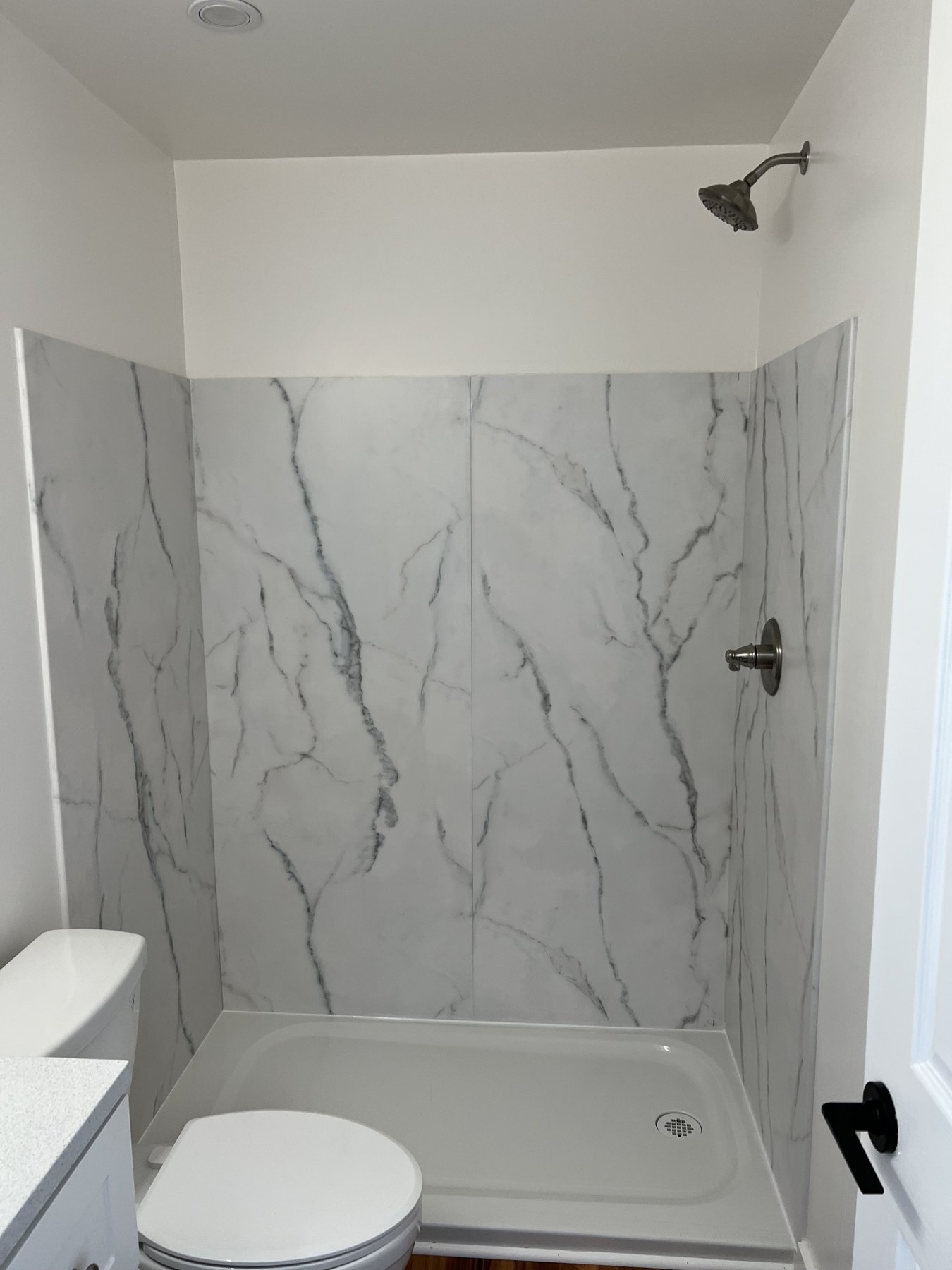 Bathroom with white shower surround and marble-patterned wall panels