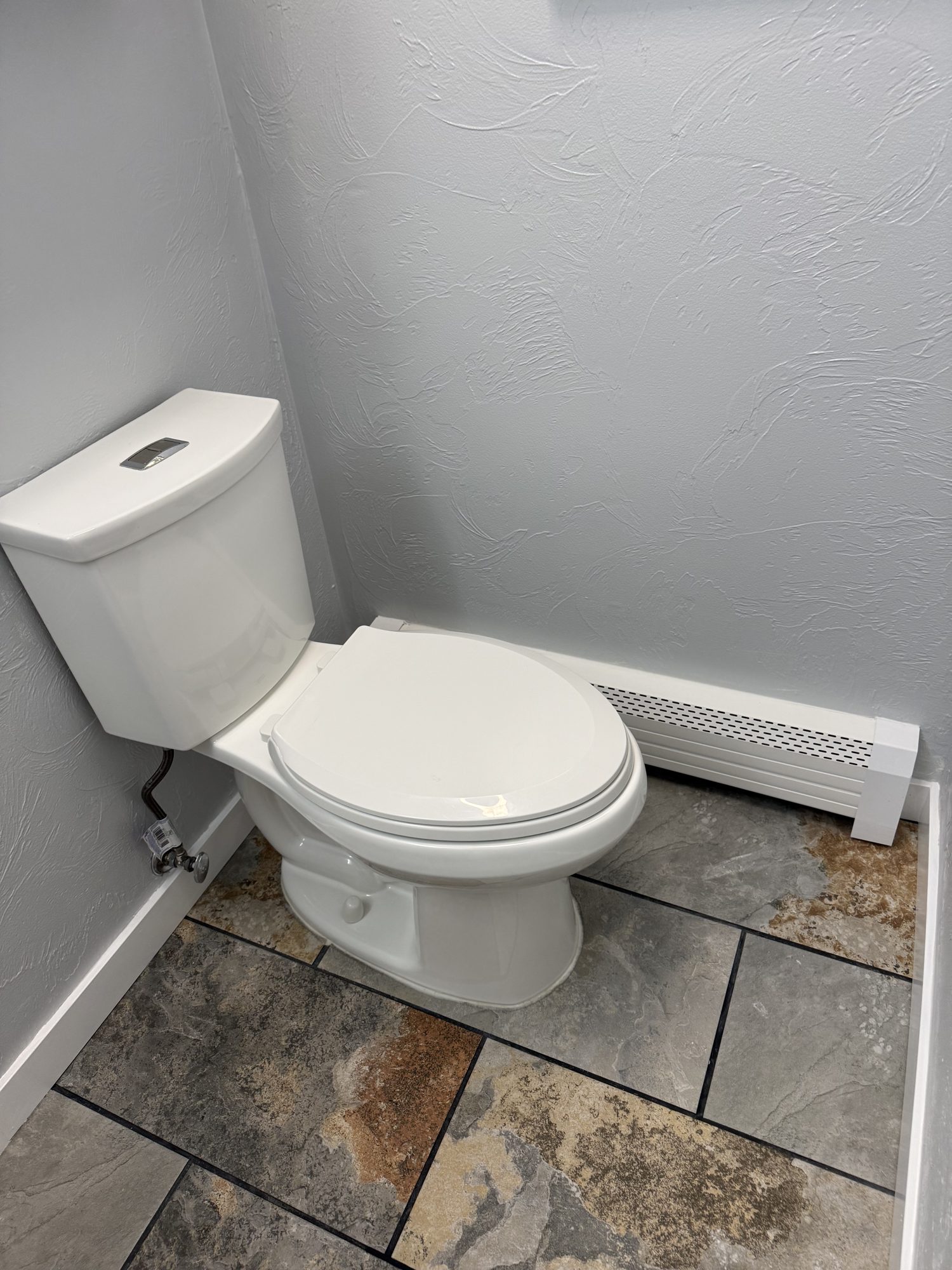 Bathroom update with a white toilet, gray walls, and stone-look tile flooring