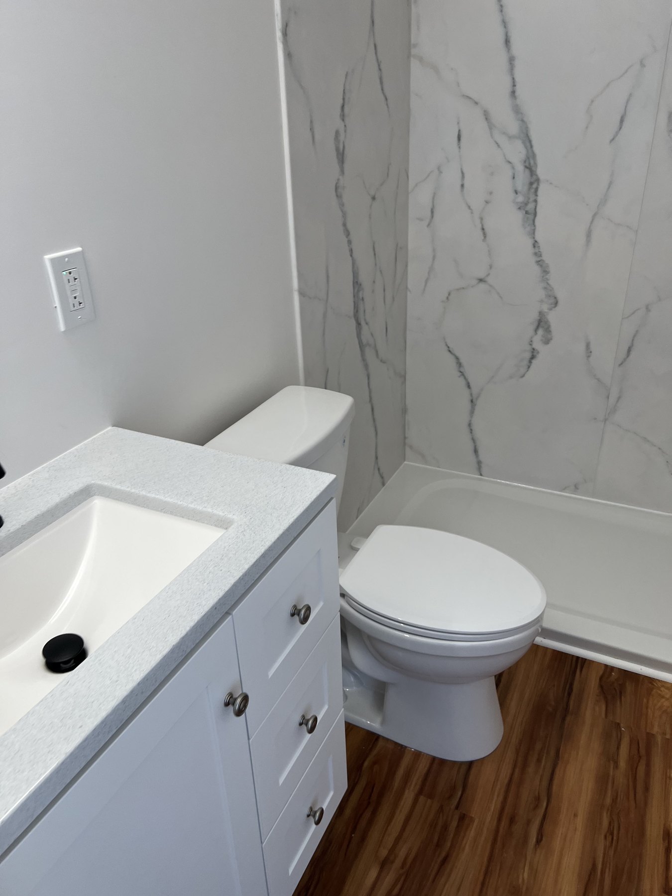 Completed bathroom vanity and toilet beside marble-patterned shower panels