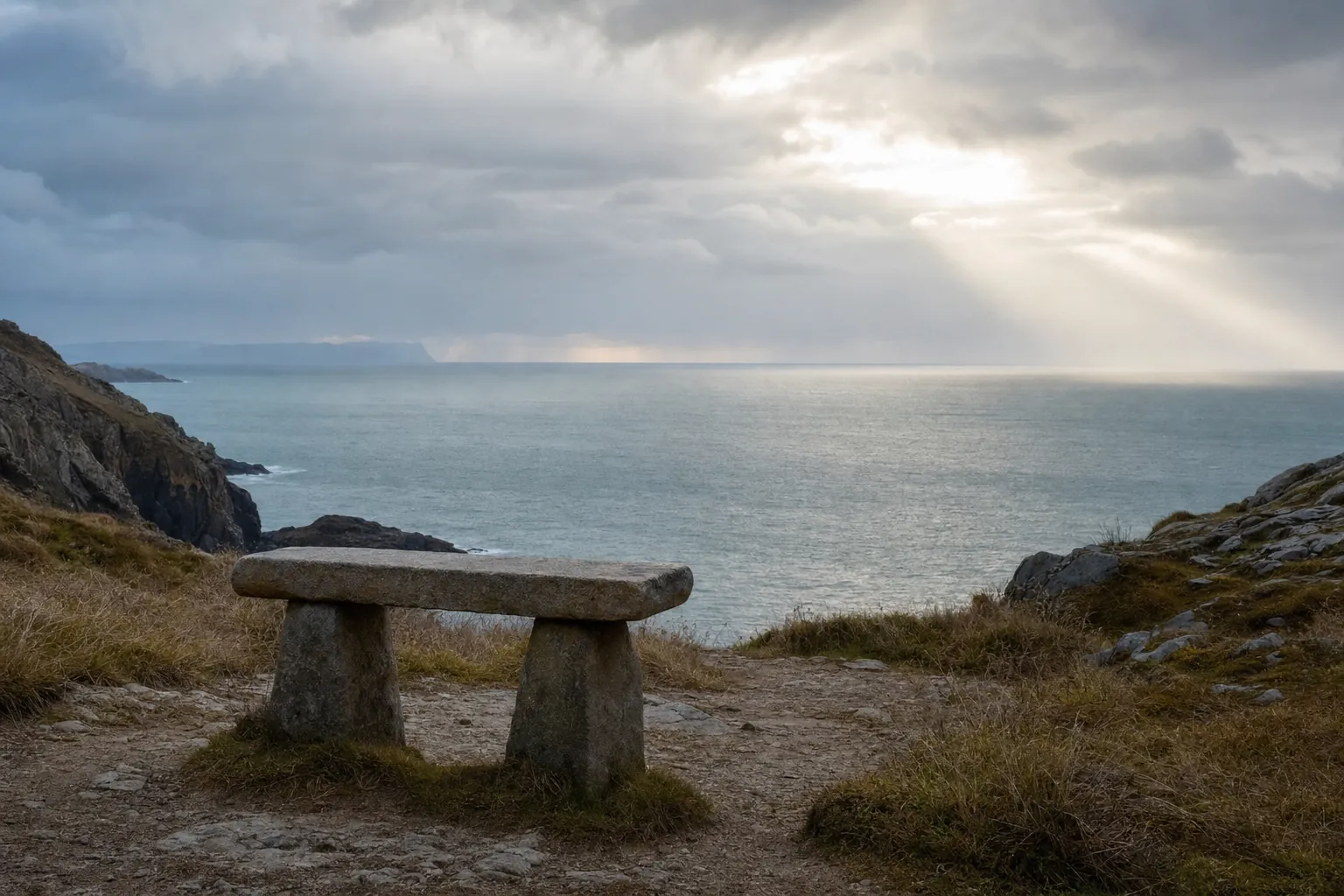 A stone bench on a coastal path looking out toward a cloudy sea