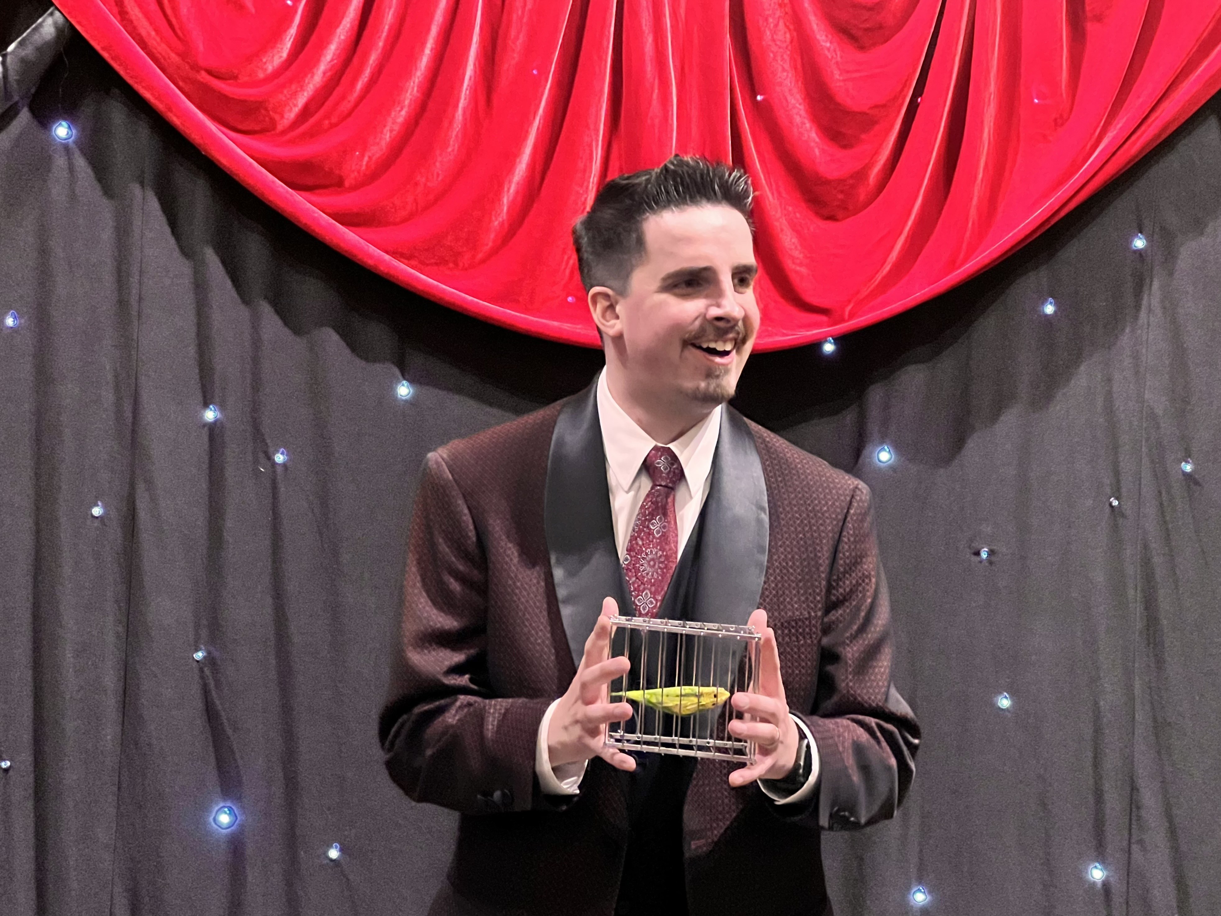 Neal Chamberlain holding a small birdcage during a live stage performance