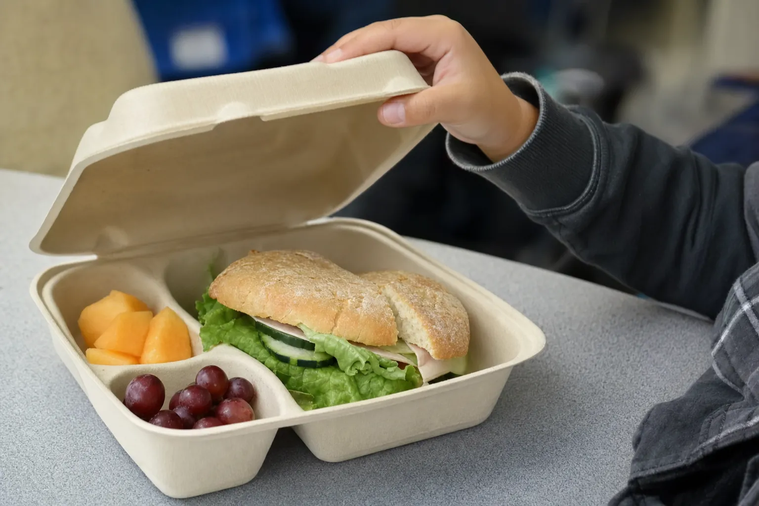Student opening a restaurant-prepared meal in a molded fiber clamshell.