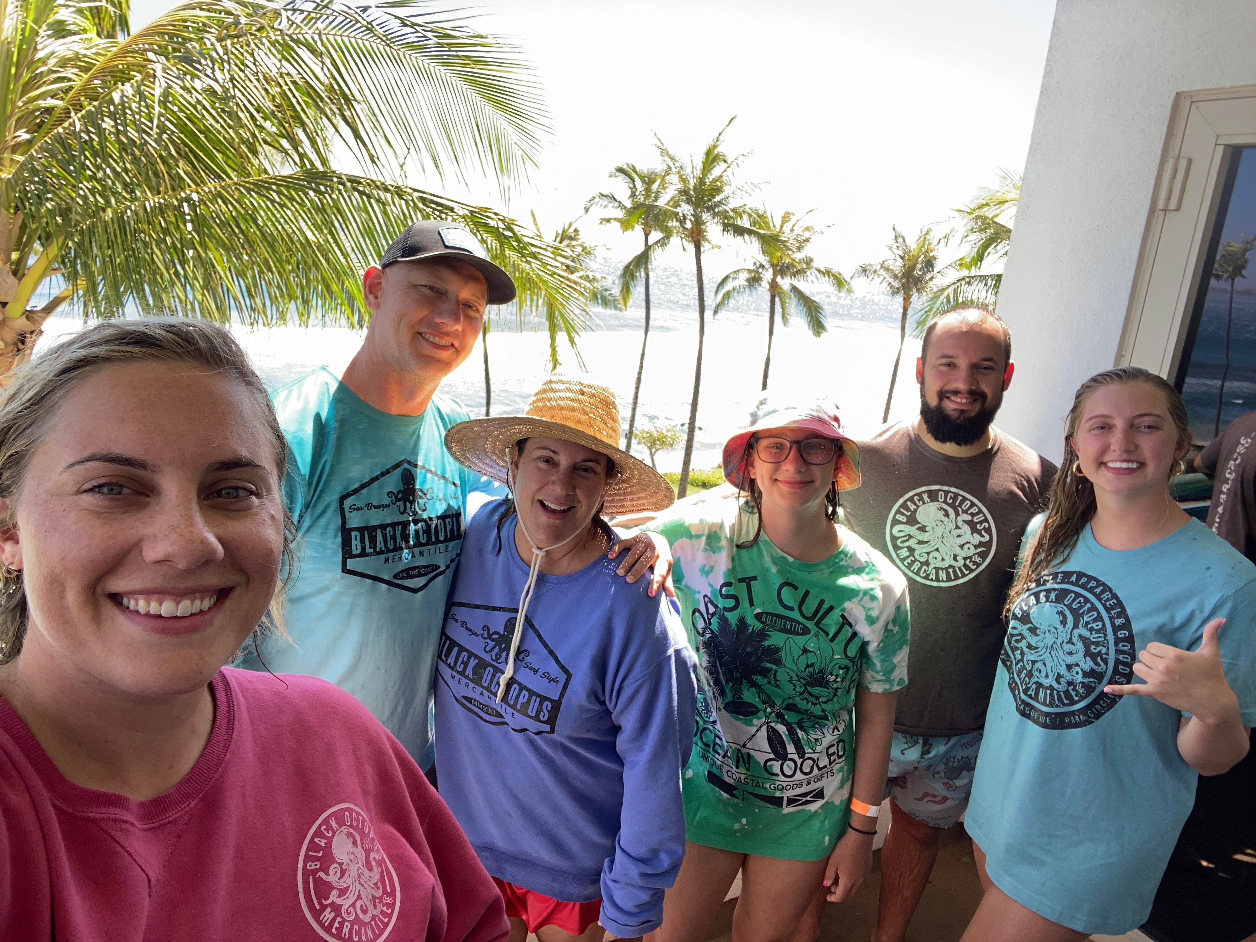 Six people wearing Black Octopus coastal apparel beside palm trees and the ocean
