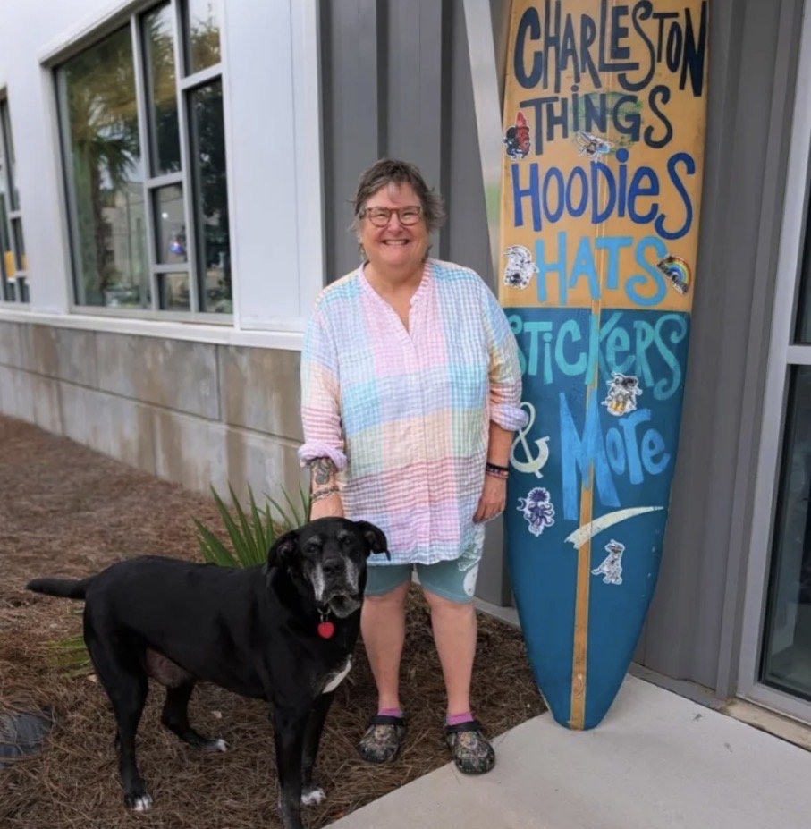 Missy and a black dog outside Black Octopus Mercantile beside a colorful surfboard sign