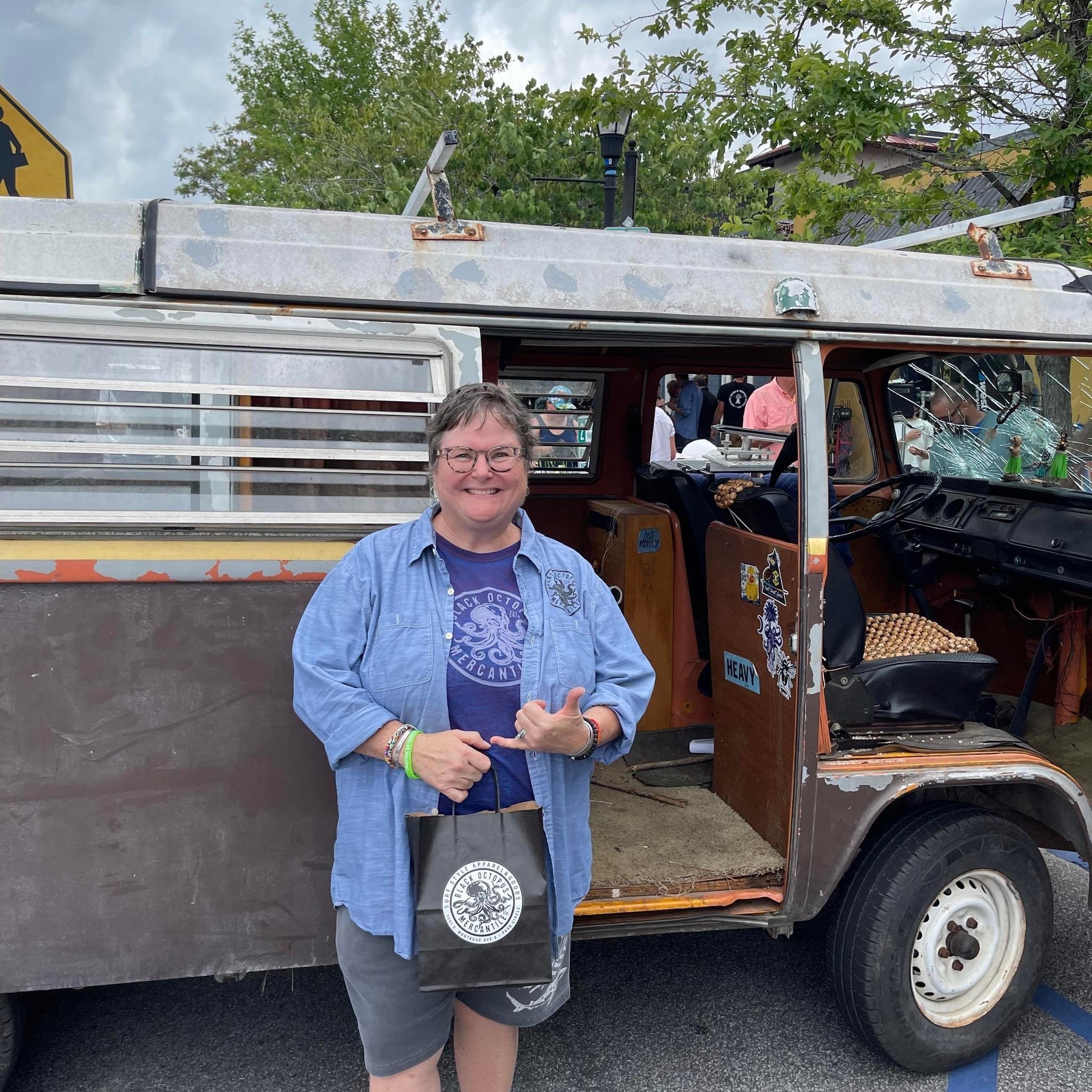 Black Octopus Mercantile artist wearing branded apparel and holding a shop bag beside a vintage van