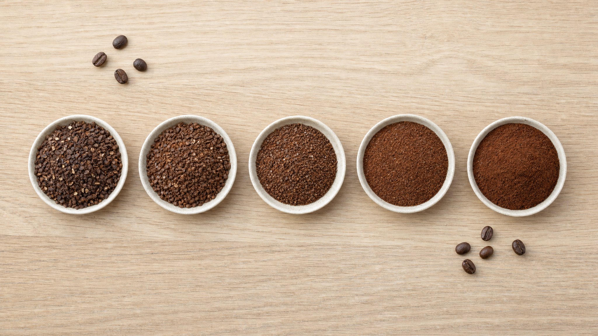 Five bowls of coffee grounds progressing from coarse pieces to a fine powder