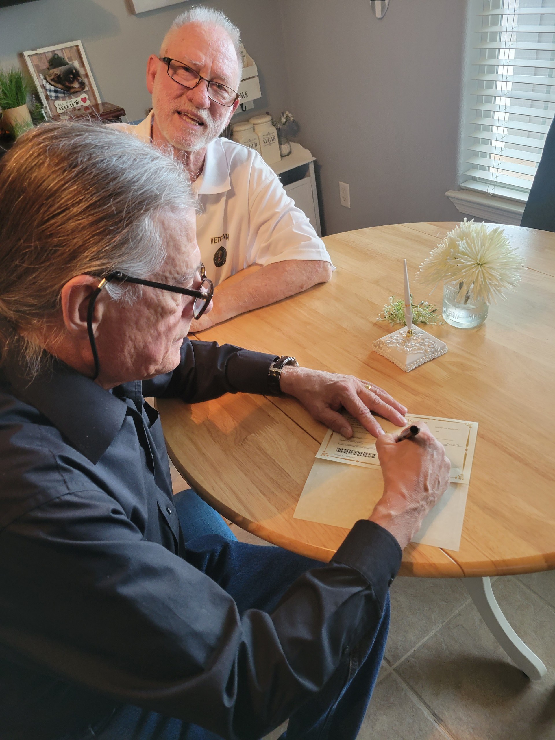 A groom signing the marriage license at a table with Edward