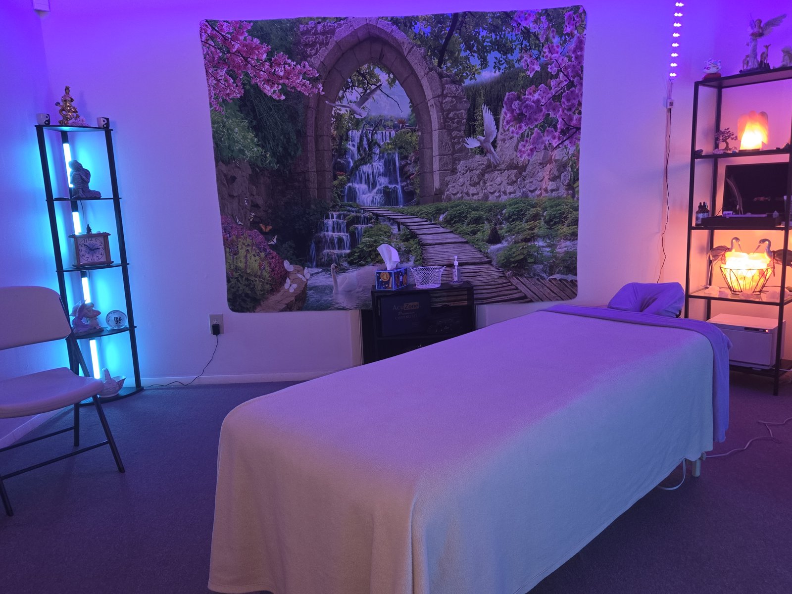 Lisa’s massage table with a cherry-blossom waterfall tapestry and softly lit shelves