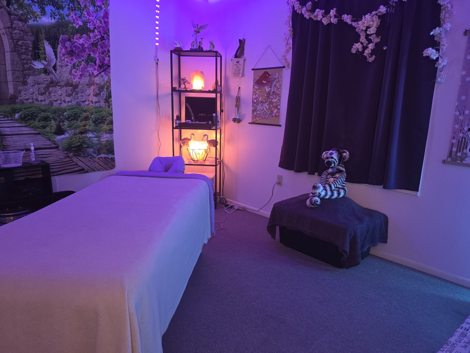 The treatment room with purple lighting, a massage table, and cherry-blossom window decor