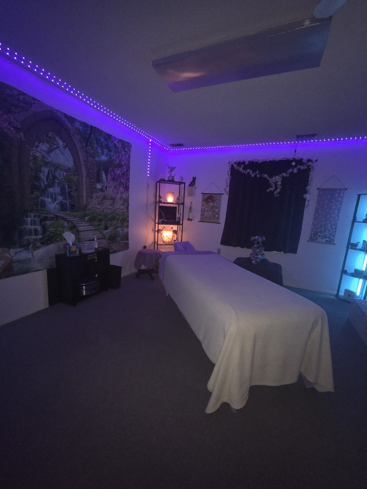 A full view of the massage room with purple accent lighting and a prepared massage table