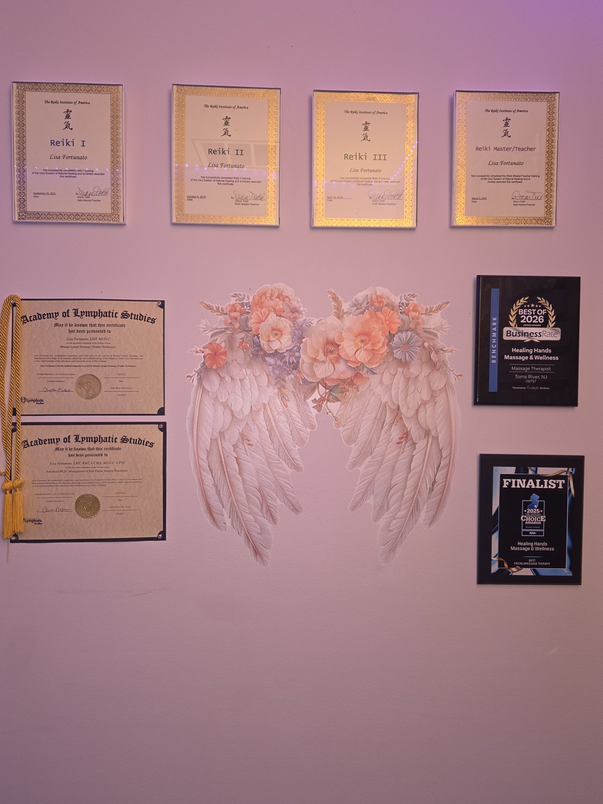 Lisa Fortunato’s framed Reiki and lymphatic studies certificates alongside floral wings and award plaques