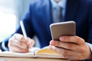 Person holding a smartphone while writing notes