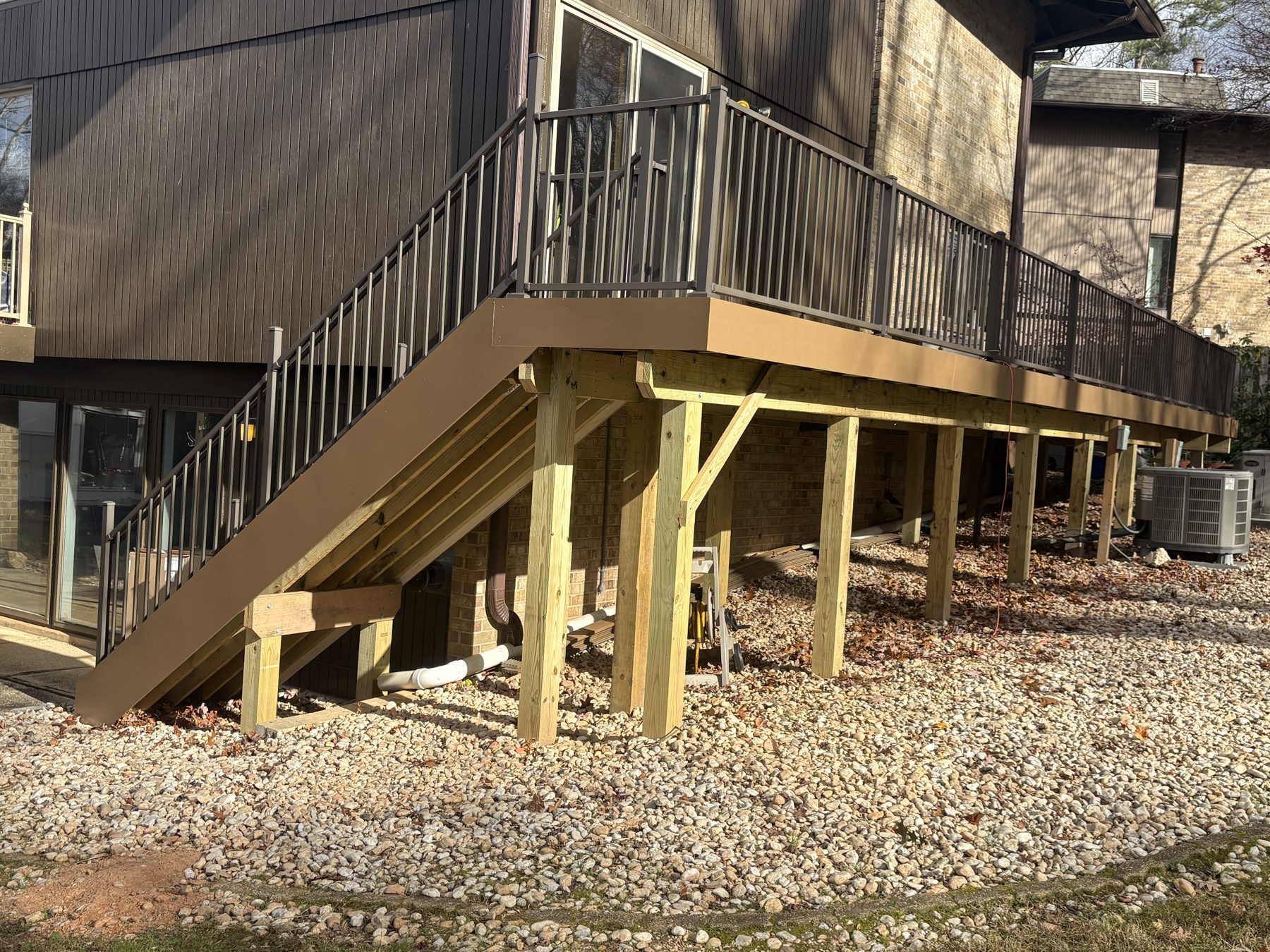 Raised brown deck with stairs and dark railings beside a brick home