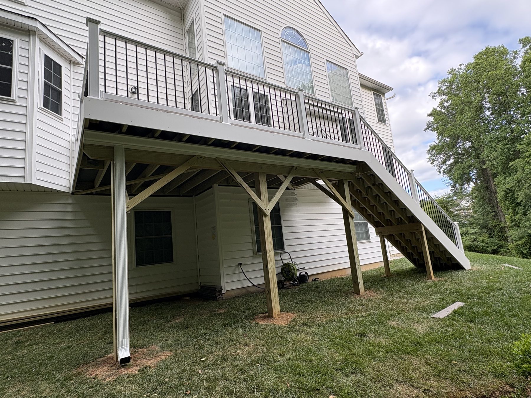 Raised deck with white railings and stairs beside a white-sided home