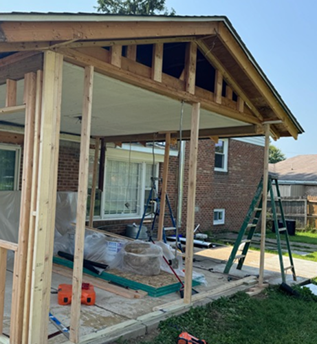 Timber porch roof under construction beside a brick home
