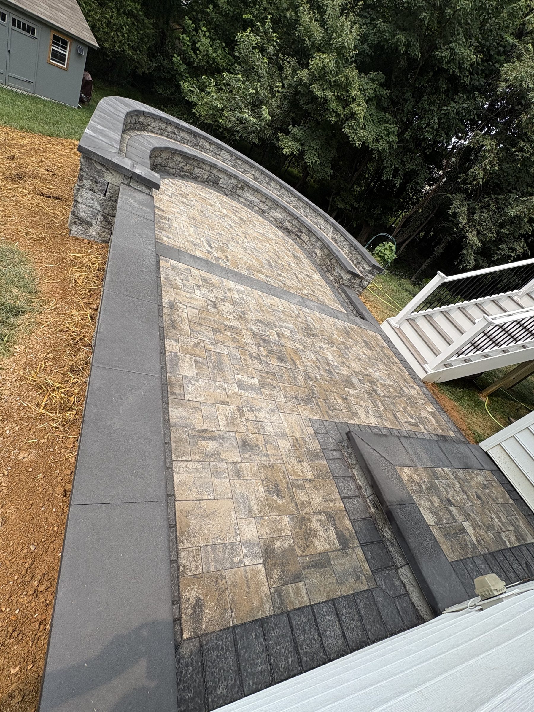 Finished multicolor paver patio with dark borders and a curved stone seating wall