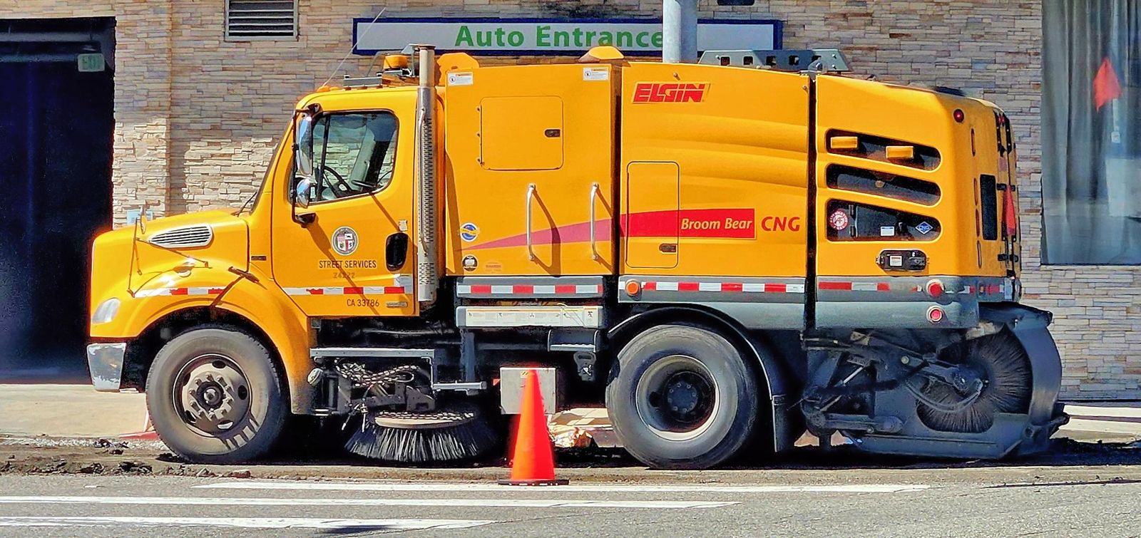 Street sweeper truck with rotating brushes alongside a city street