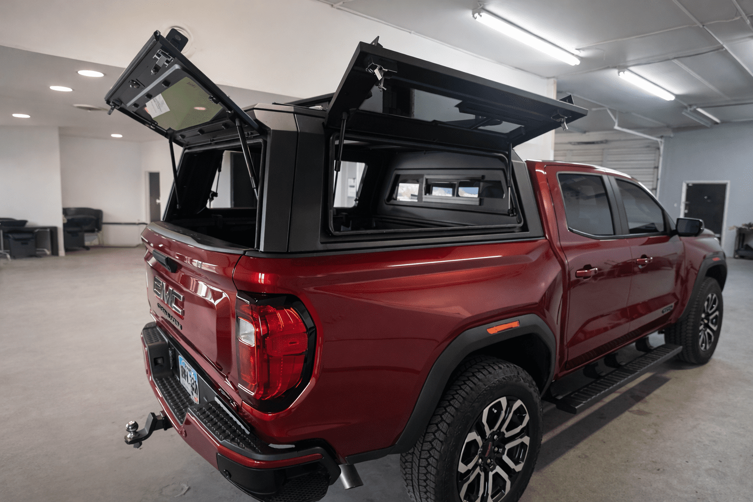 Red GMC Canyon with a black aluminum topper and open gullwing doors in the Peakline Overland installation shop
