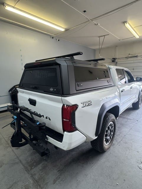 White Toyota Tacoma fitted with a black aluminum topper