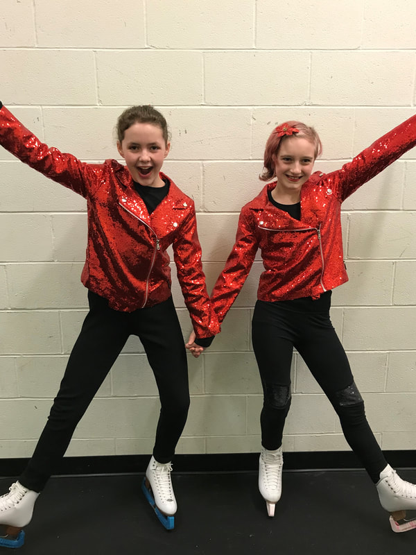 Two young figure skaters in red performance costumes