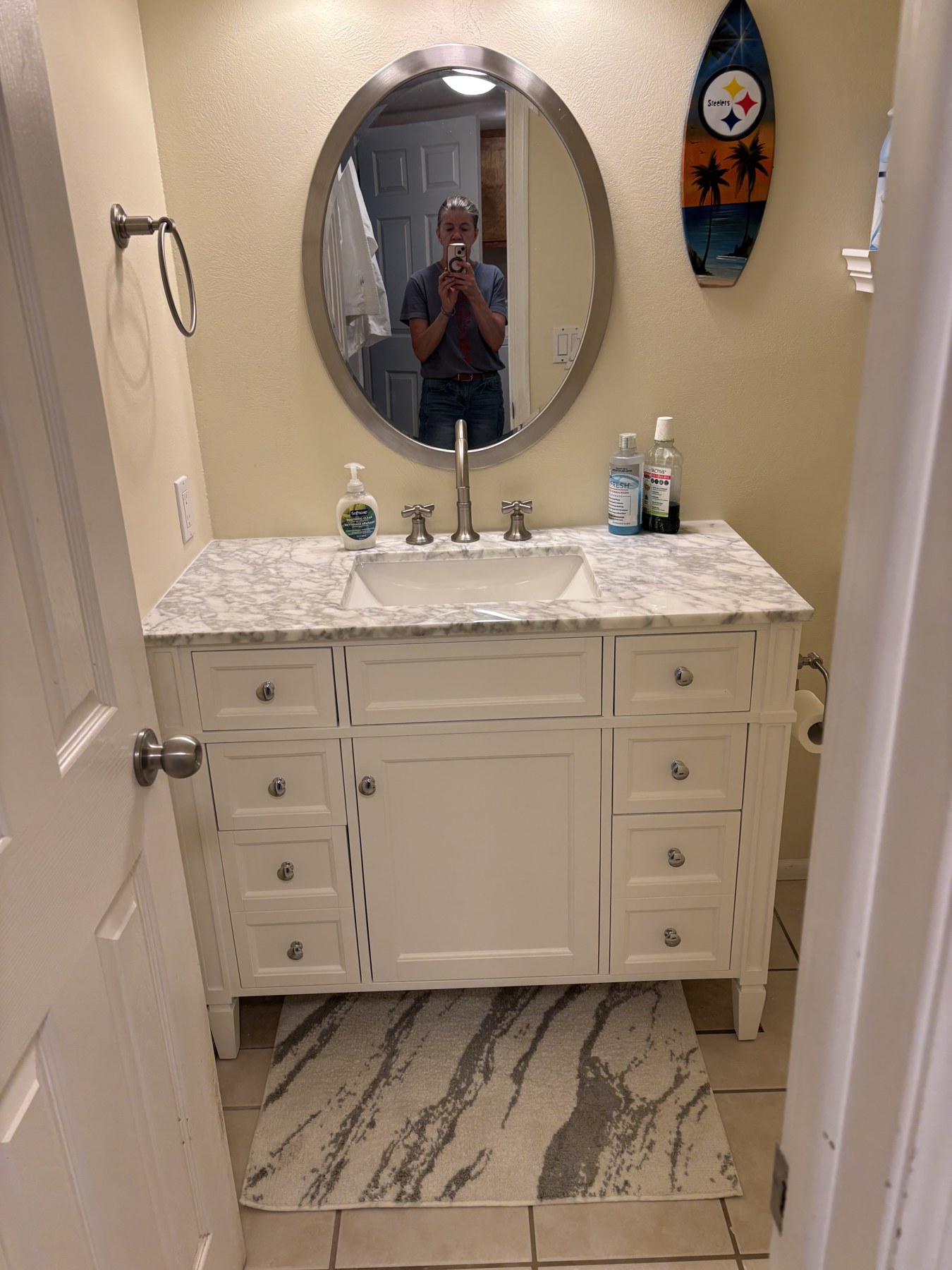 White bathroom vanity with a marble-look countertop and oval mirror.