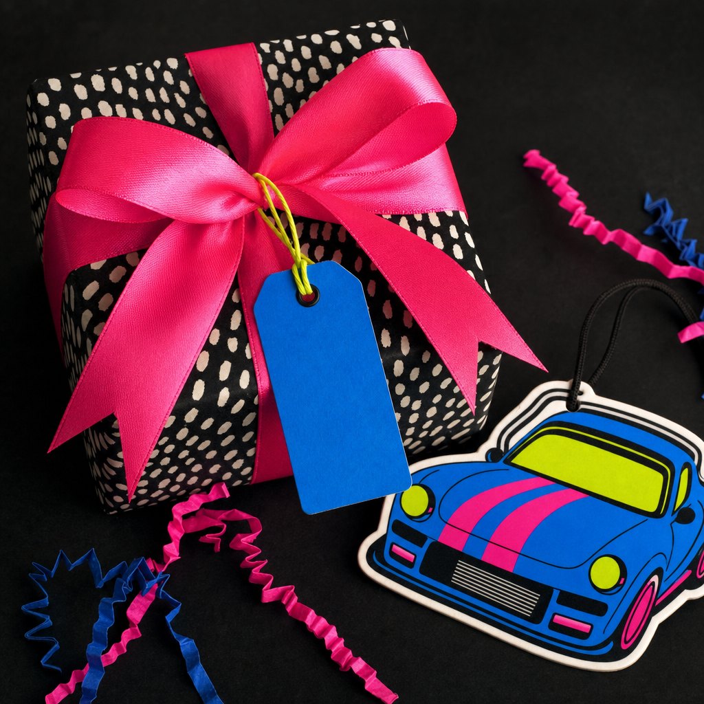 A bright pink wrapped gift with a colorful car freshener